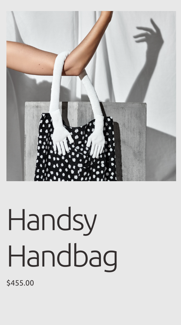 A black and white polka dot handbag with white knit arm handles hanging from a concrete block, with a woman's arm holding the bag. The background is light-colored with shadows on the wall.