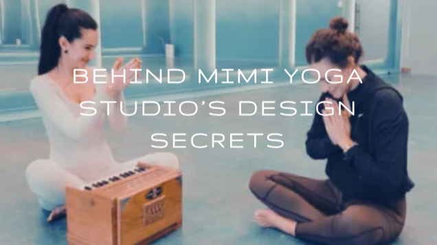 Two women sitting cross-legged on a yoga studio floor, engaging in a meditation or yoga session, with a wooden instrument placed between them, and text overlay reading 'Behind Mimi Yoga Studio's Design Secrets'.