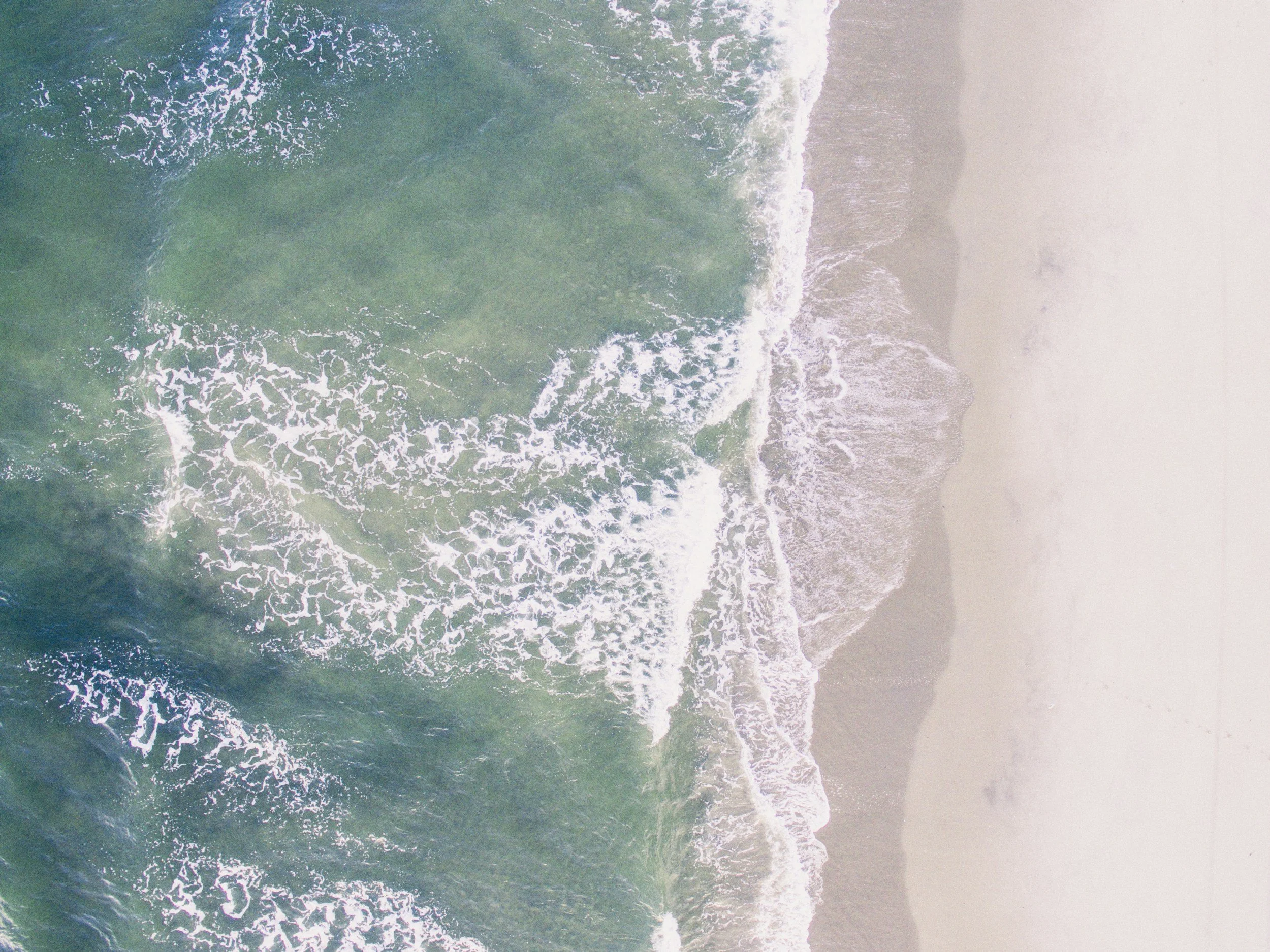 Aerial view of ocean waves crashing onto sandy beach shoreline.