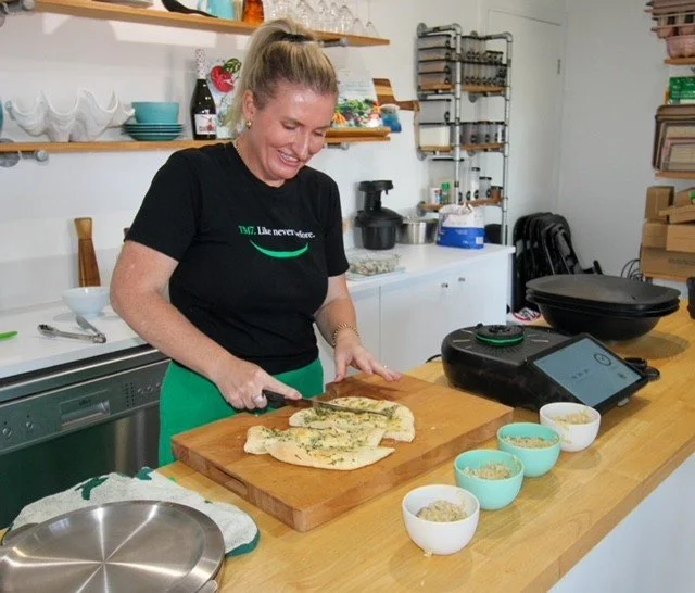 Woman slicing flatbread or pizza dough in a kitchen with various bowls and cooking equipment