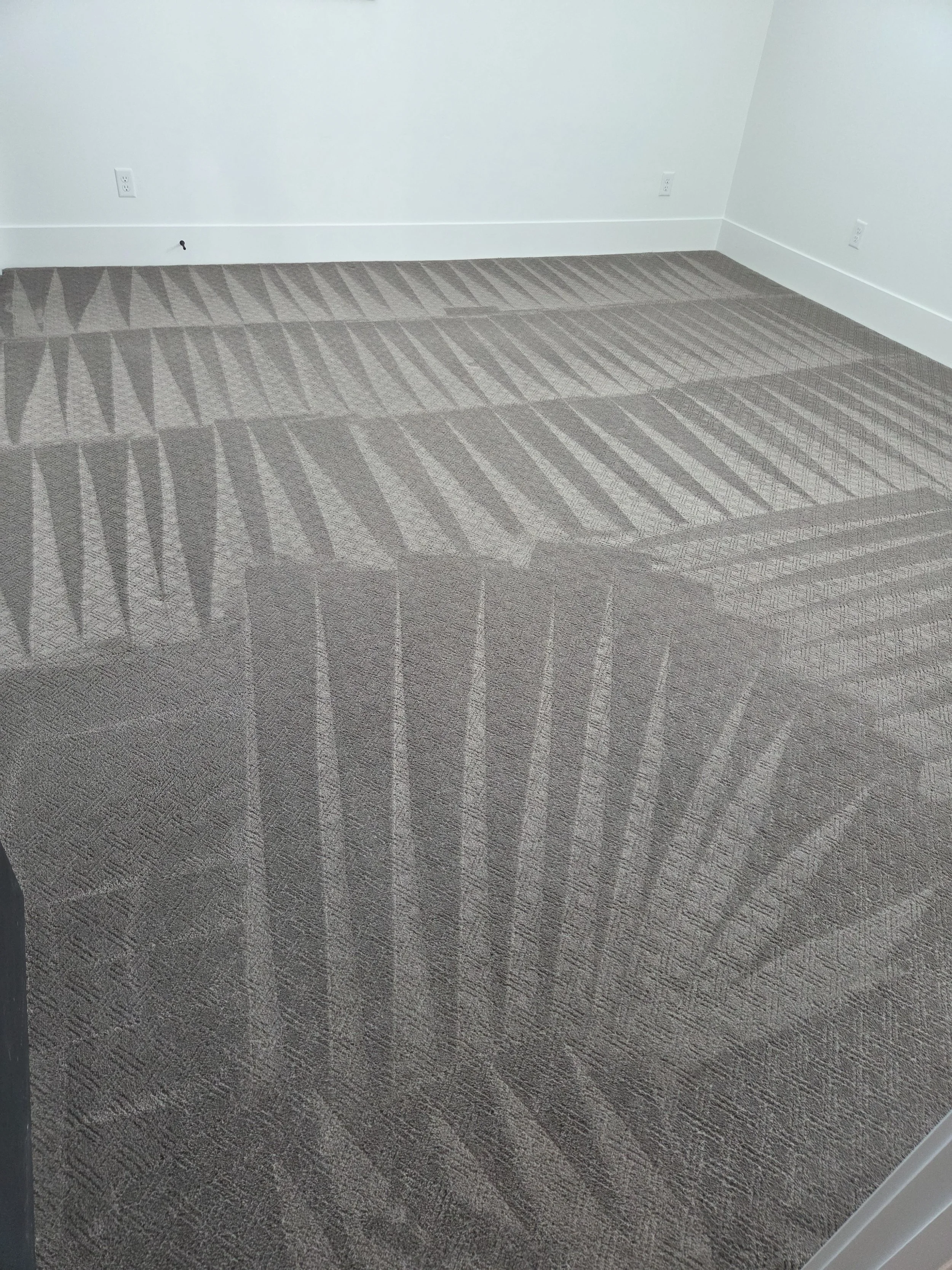 Empty room with beige carpet and white walls, electrical outlets visible along the walls.