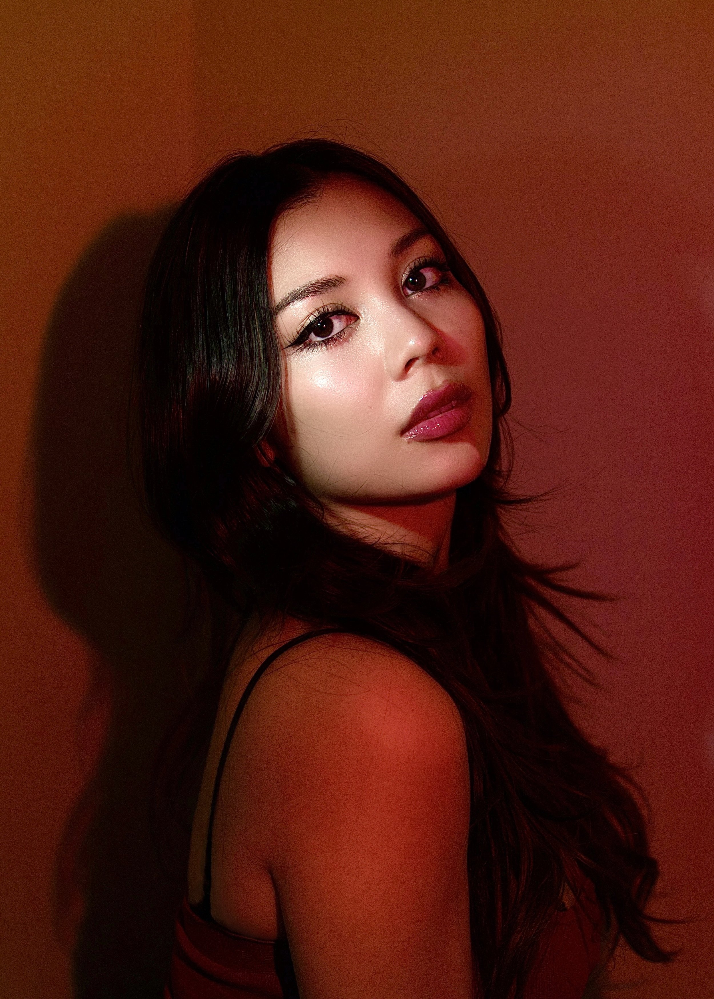 A woman with long dark hair looking at the camera against a red background.
