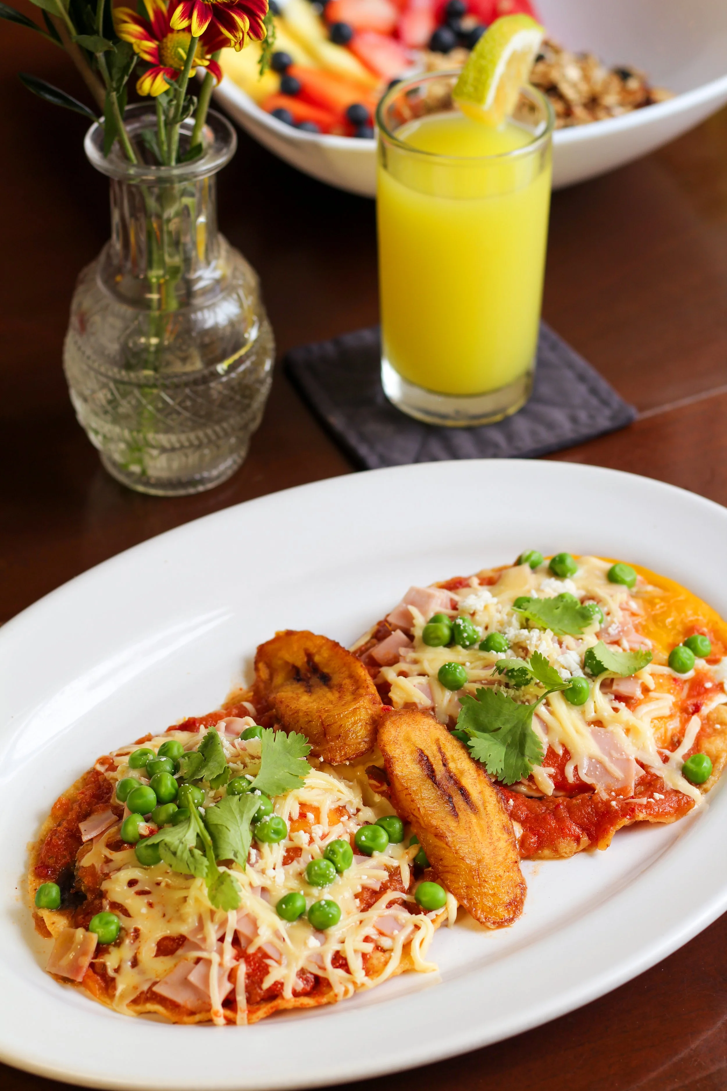 Huevos motuleños, jugo de naranja, flores en un jarrón.