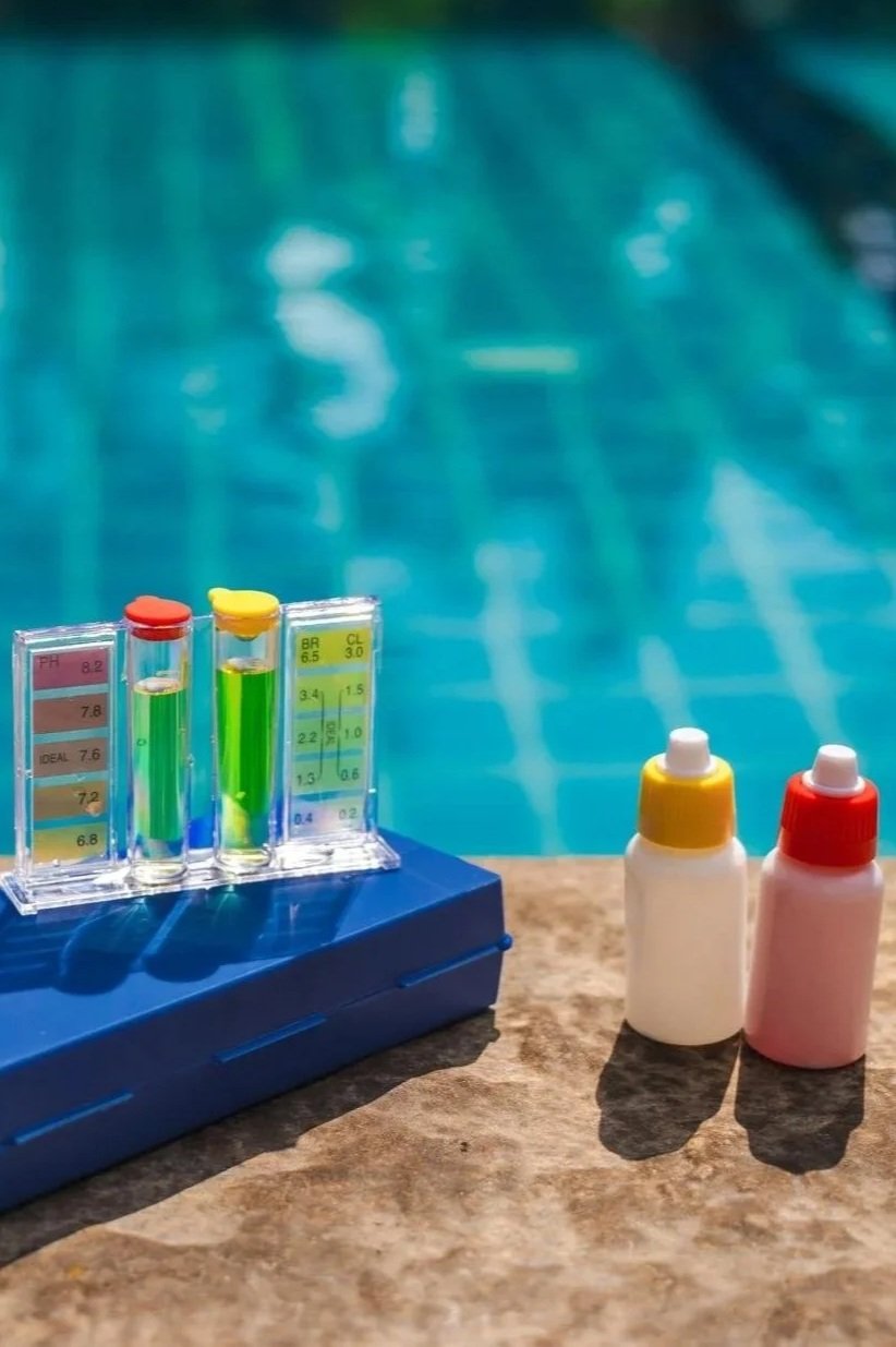 Testing equipment with test tubes and dye bottles on a poolside surface near the water.