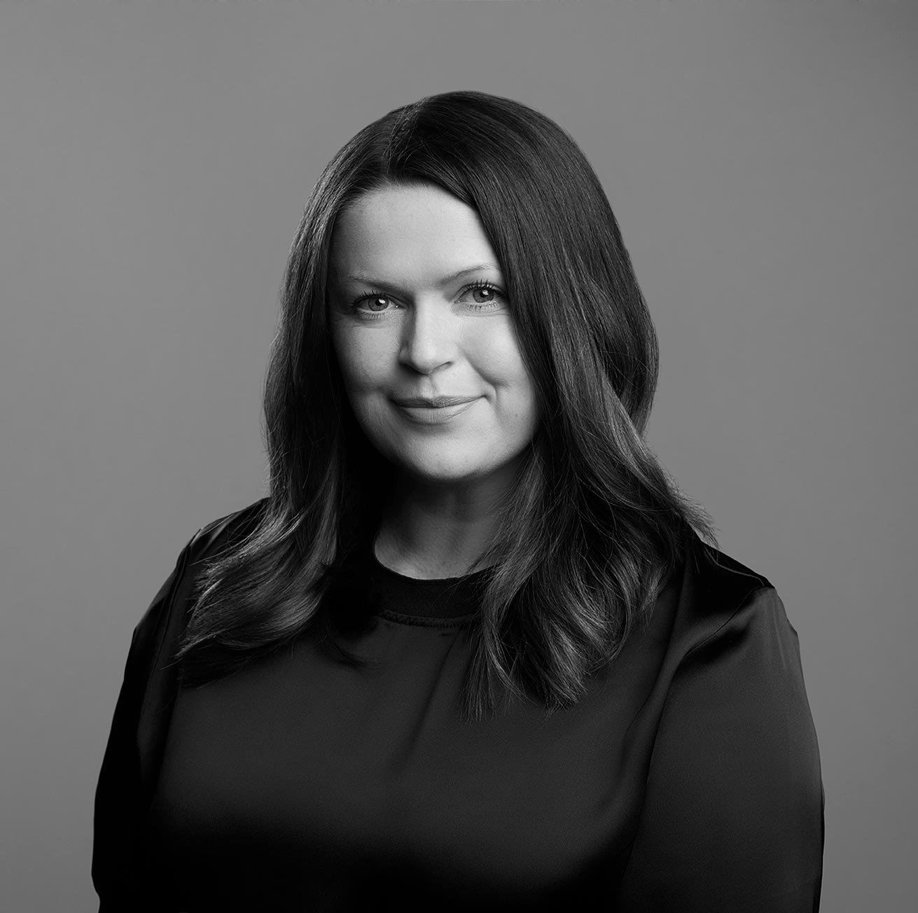 Black and white portrait of Fiona Dall with shoulder-length hair, smiling, wearing a dark top, against a plain background.