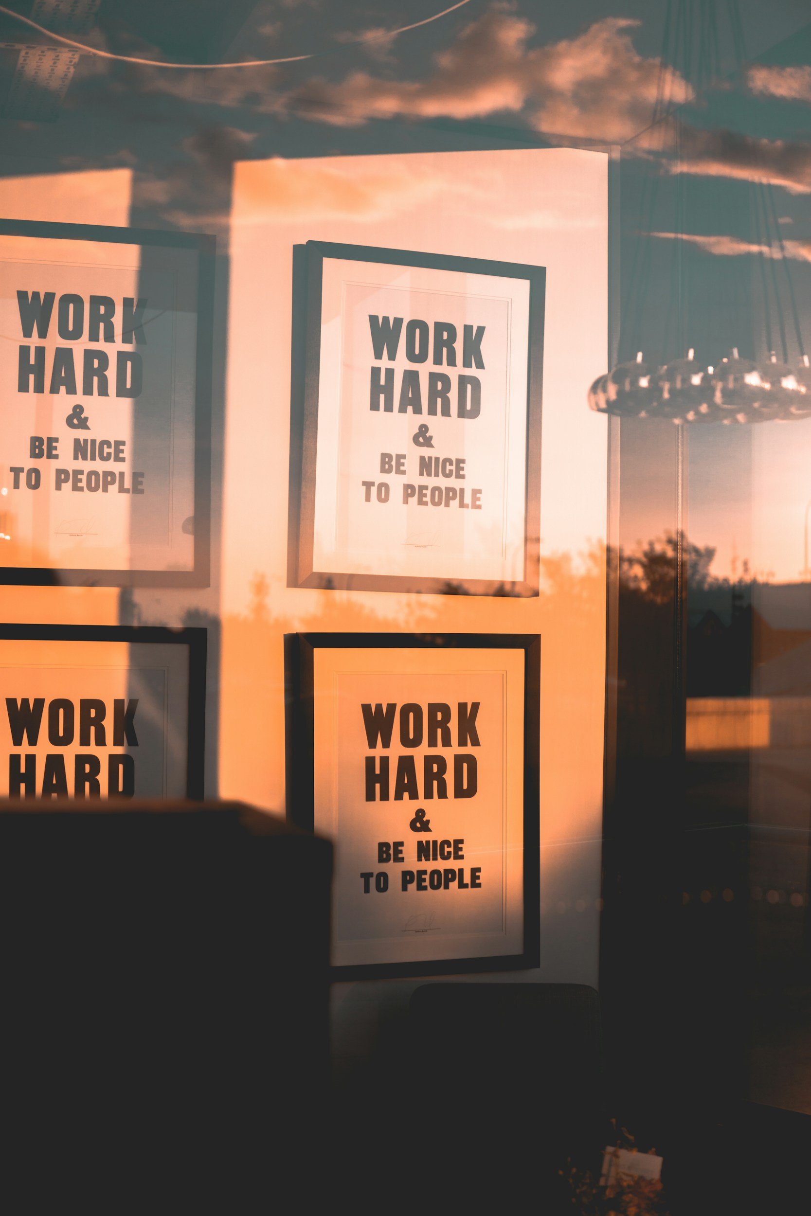 Sunset view through a window showing posters with motivational text: 'WORK HARD & BE NICE TO PEOPLE'.