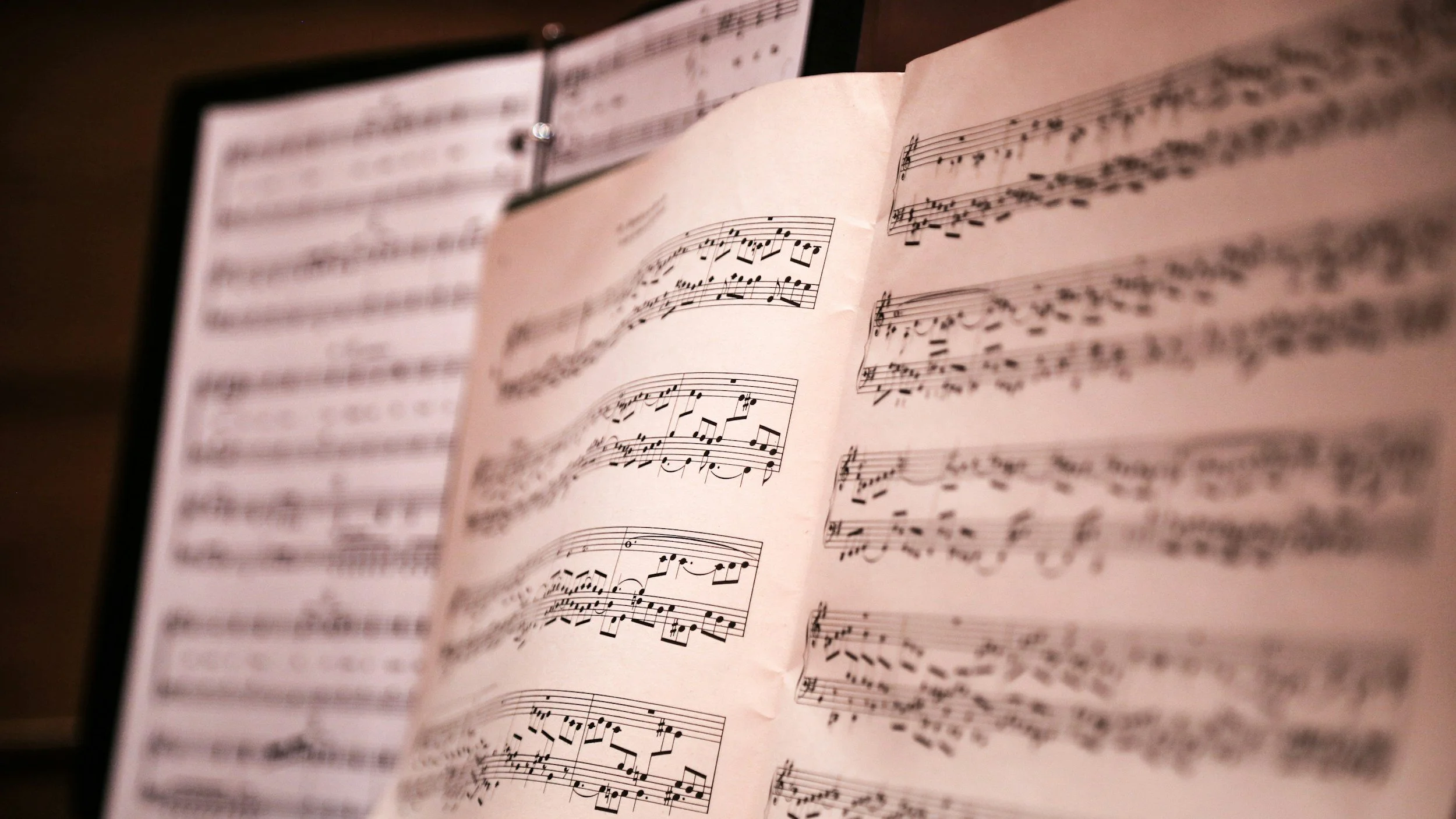 Close-up of an open sheet music book with musical notes and staff lines, slightly curled pages, on a music stand.