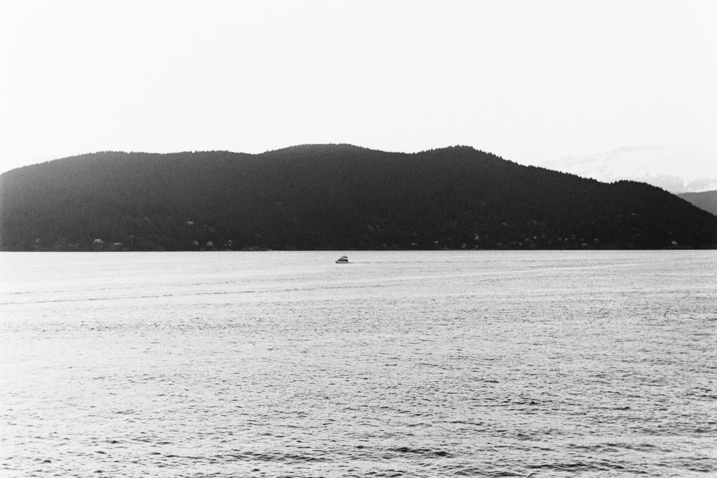 Calm body of water with a small boat and a distant mountain range in the background, in black and white.