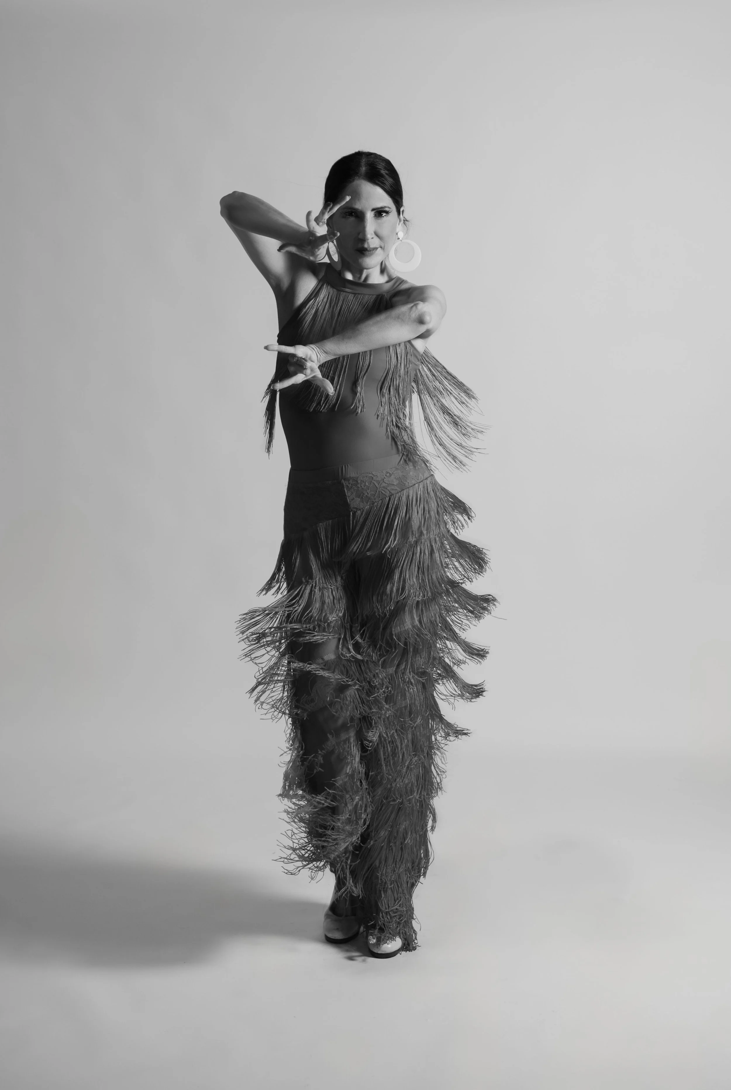 Female dancer in fringe costume performing a dance pose in a studio.