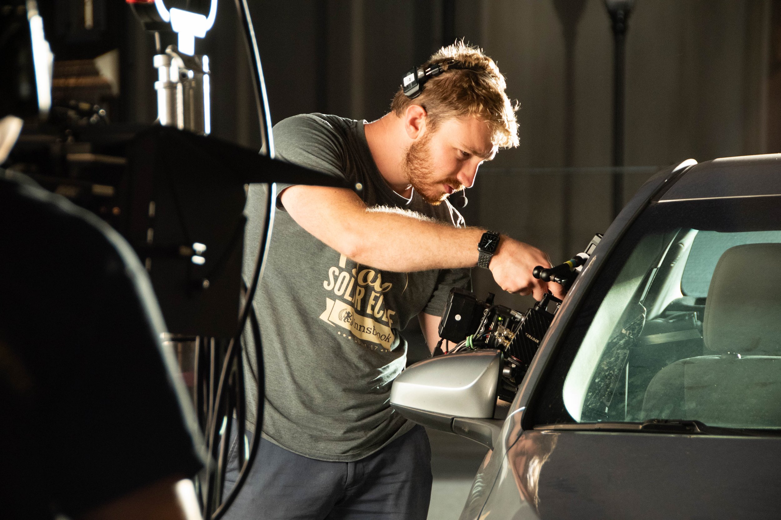 A man working on a camera setup inside a studio, focusing intensely on the equipment next to a car.