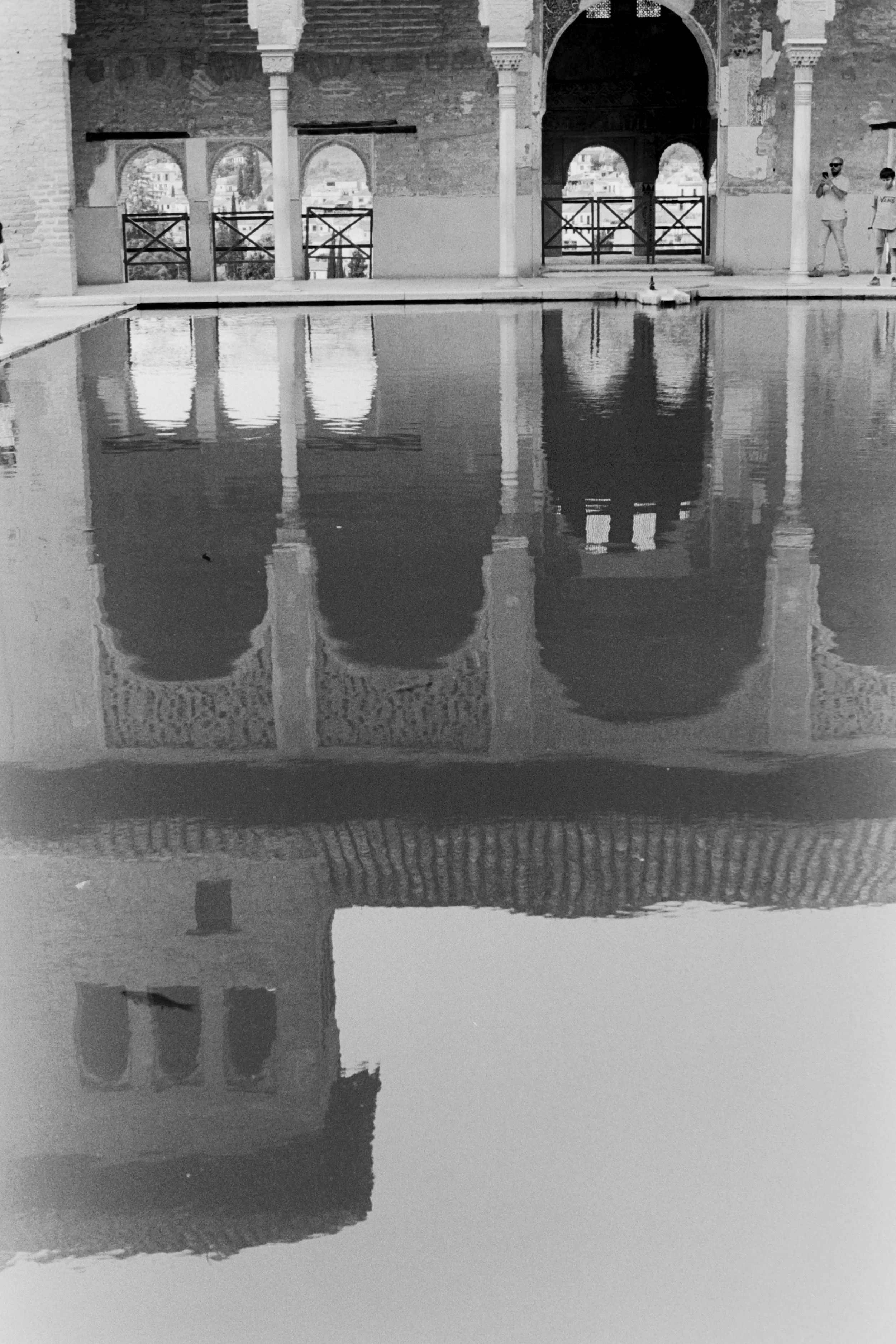Reflection of an arched historic building with domed towers in a pool of water, black and white photograph.