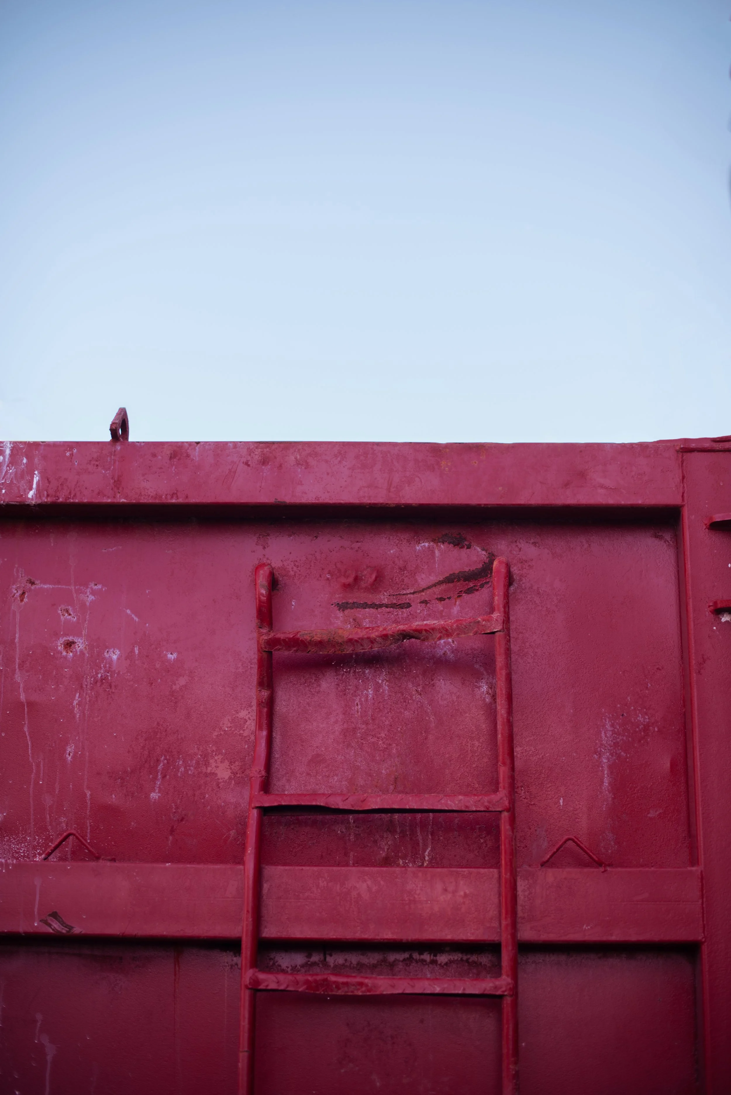 A red metal structure with a ladder against it, set against a clear sky.