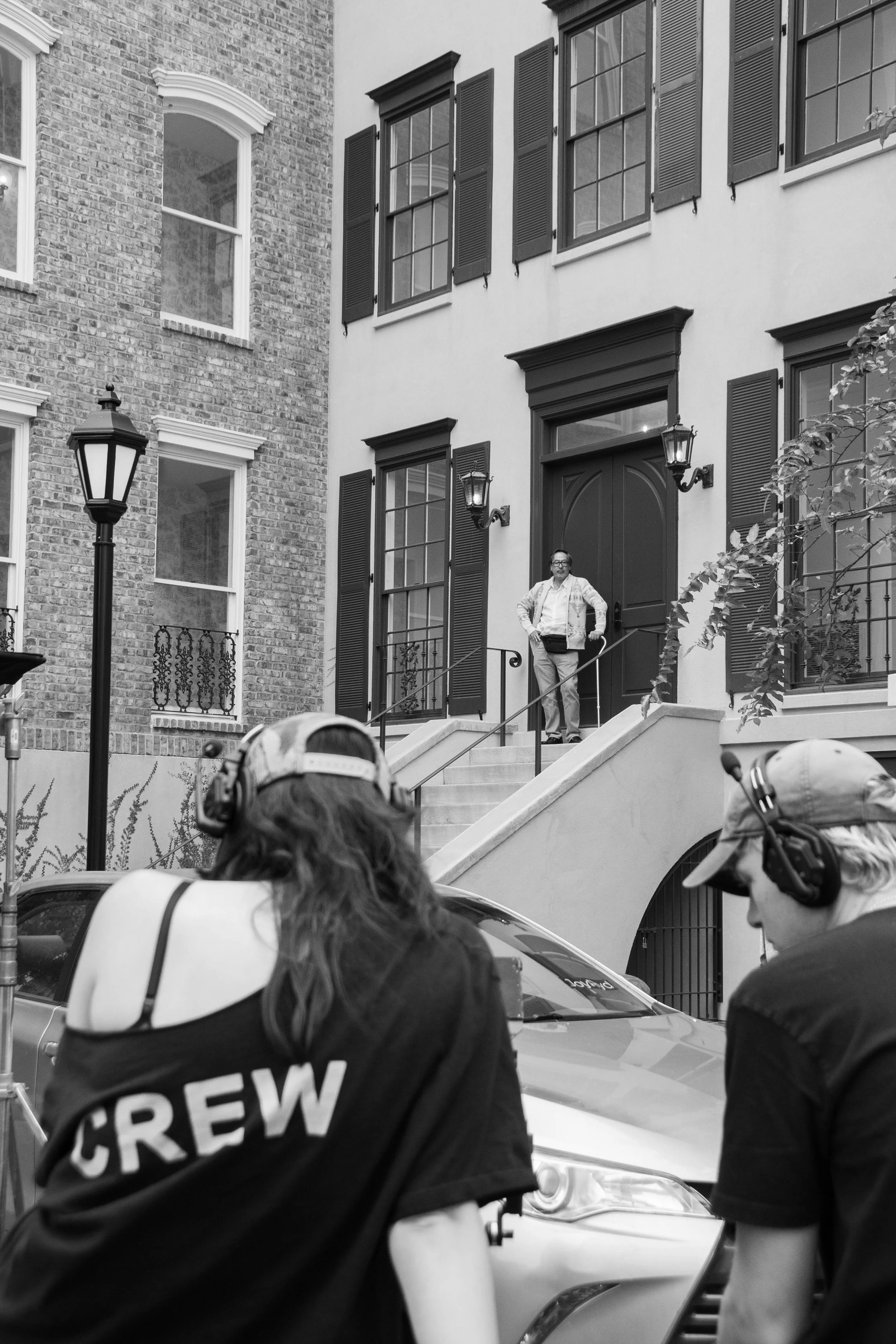Film crew filming a man standing on stairs outside a residential building.