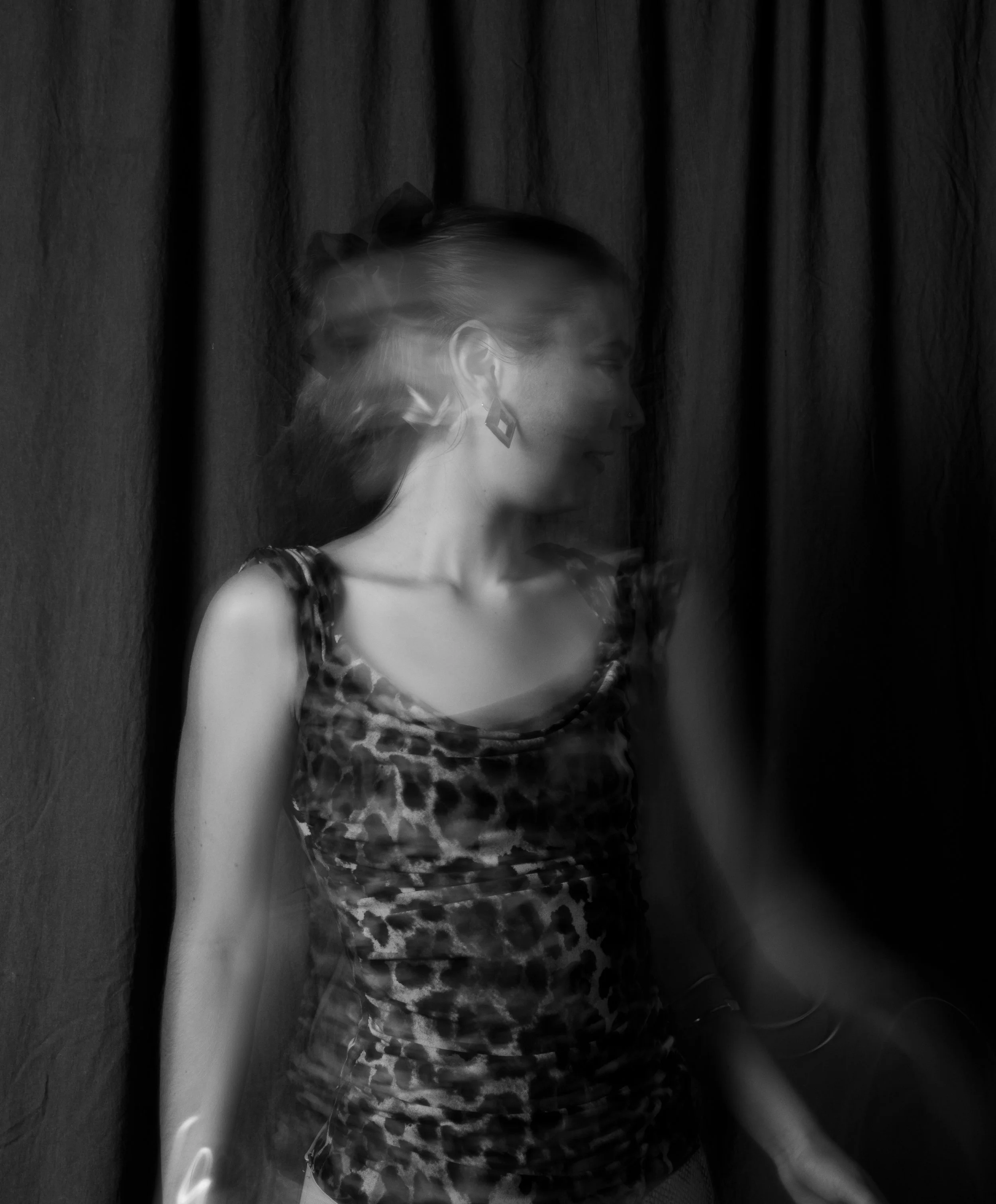 Black and white photo of a woman in a leopard print dress standing in front of a dark curtain with motion blur effect.