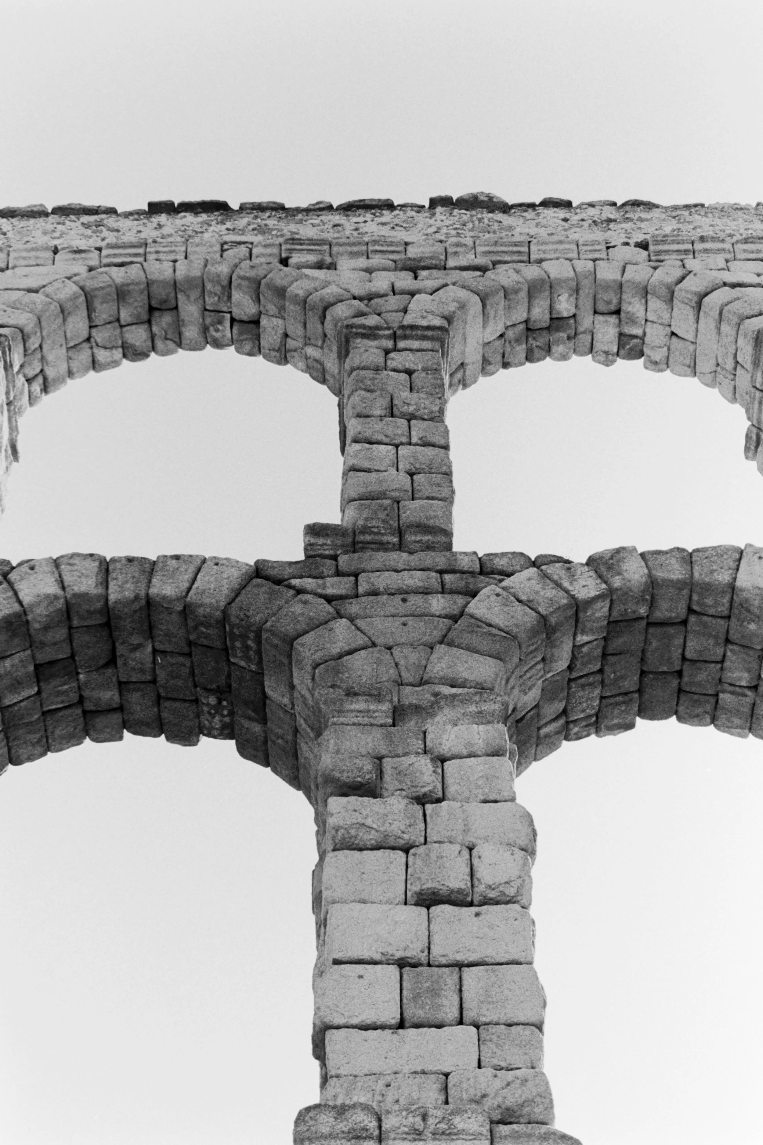 Black and white photo of an ancient stone aqueduct with arches, viewed from below.