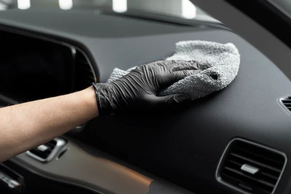 Person wearing a black glove cleaning a car dashboard with a microfiber cloth.