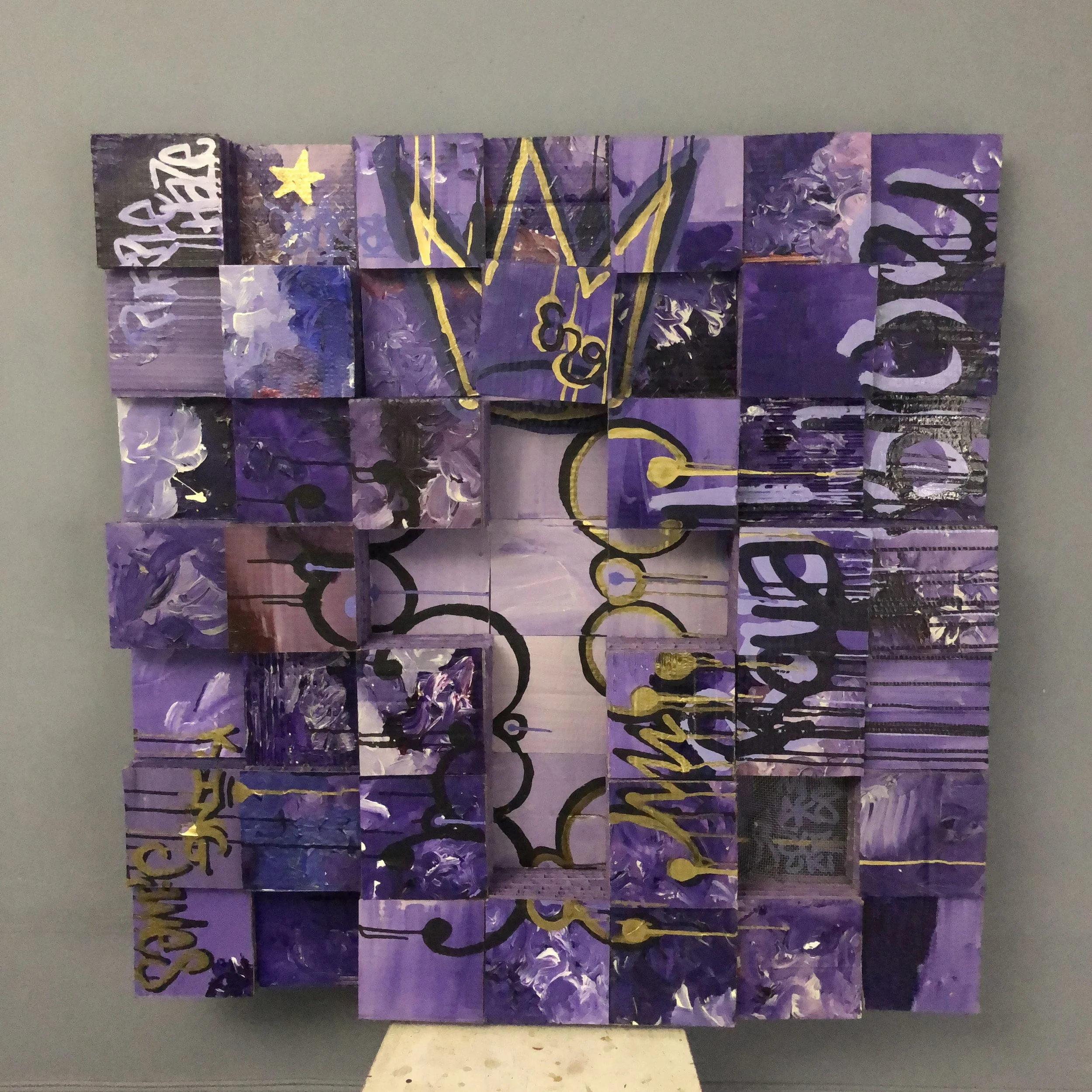A large grid using cardboard purple painted squares, a crucifix design in the center and the word "ROYAL BLUE" on the right side of piece. A gold and black crown sits on top in ink. The letters "ENG" are also painted on.