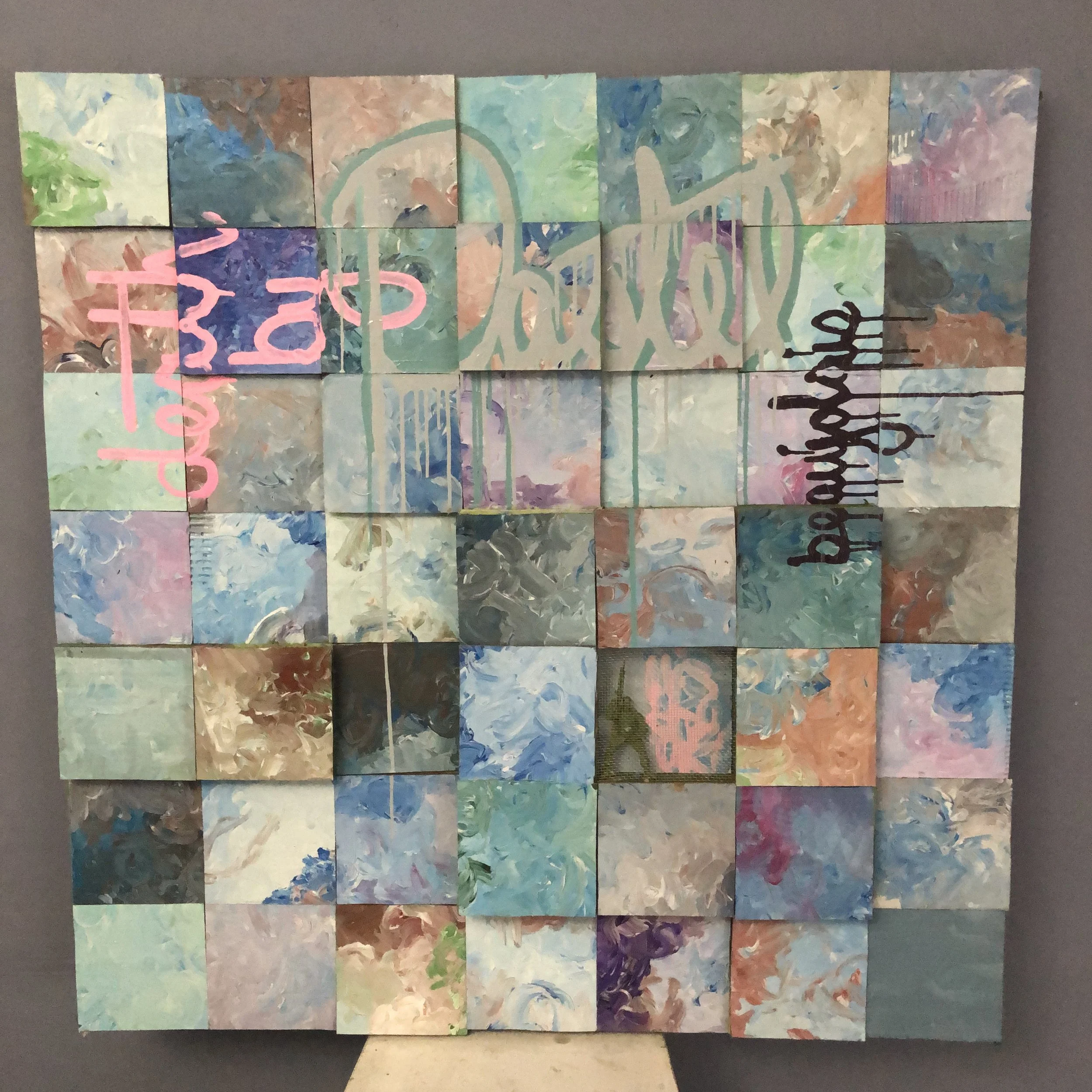 An abstract multi-colored wall art piece composed of square panels with paint swirls in pastel shades of pink, blue, green, and tan. The artwork features two handwritten words: "trust" in pink on the top left and "prolific" in black on the right side.