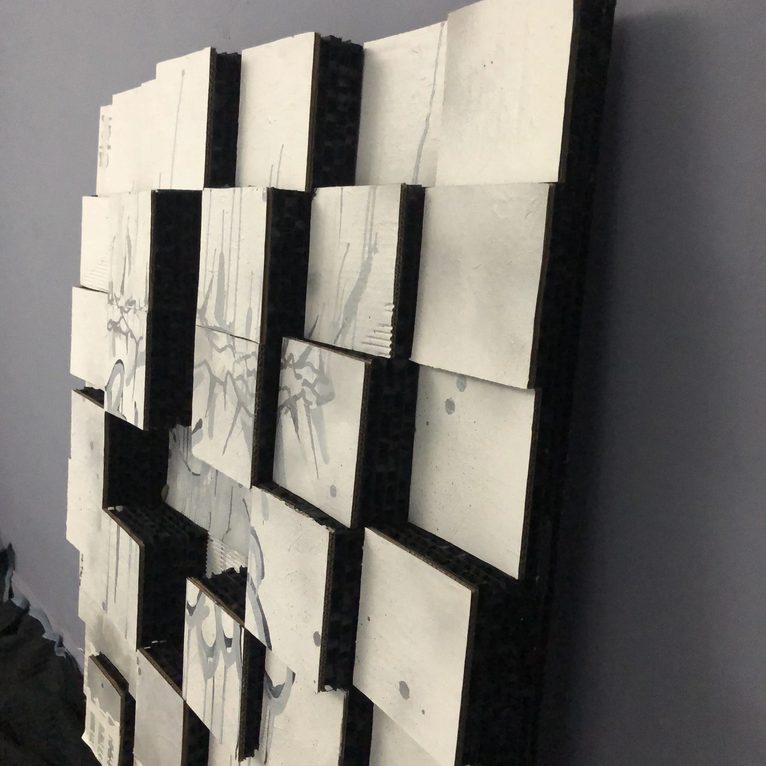 Abstract tile artwork with black and white streaks and splashes, arranged in a grid pattern on a wall.