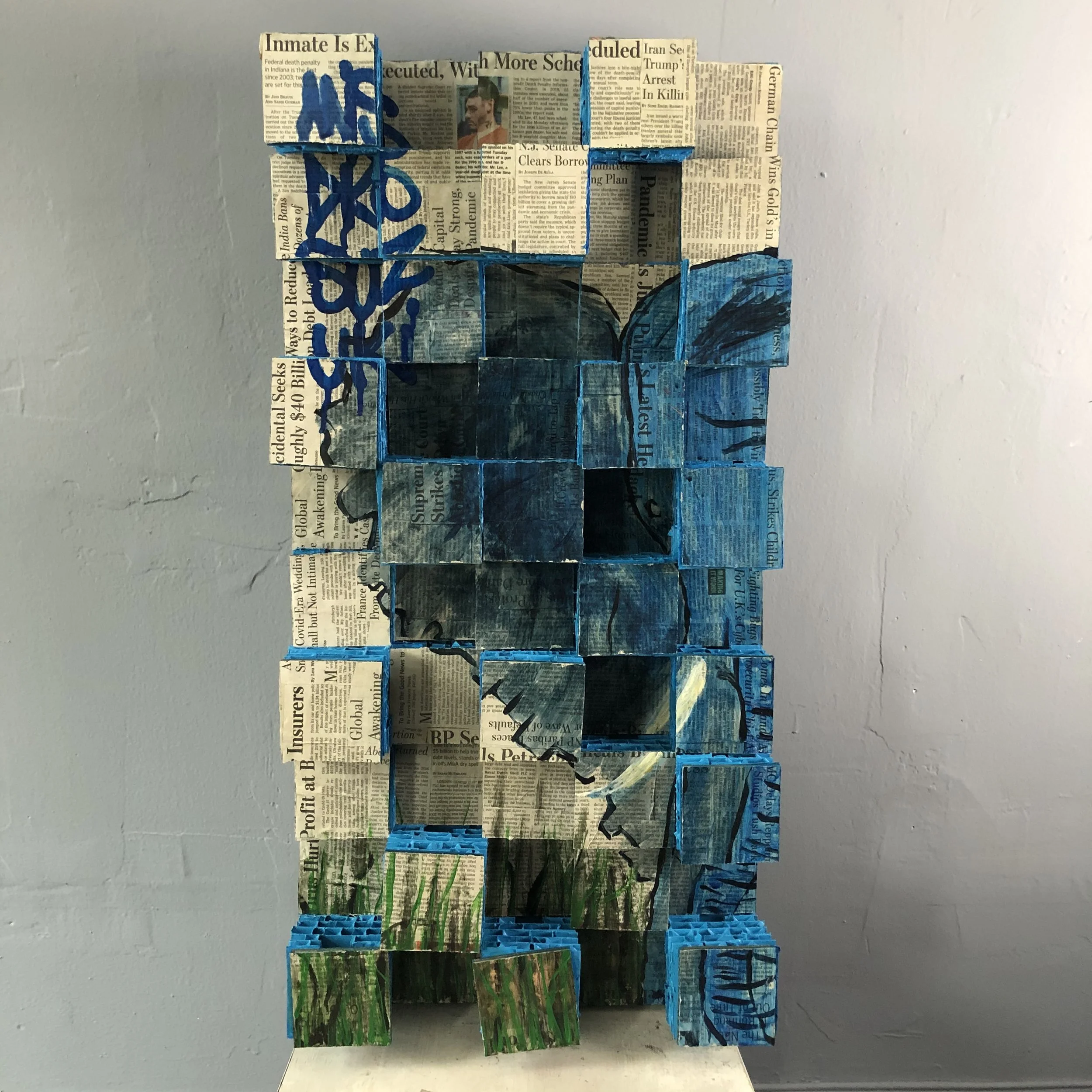 A mixed-media-collage art piece composed of newspaper-covered cardboard squares arranged in an abstract design, with a blue colored elephant in tall grass.