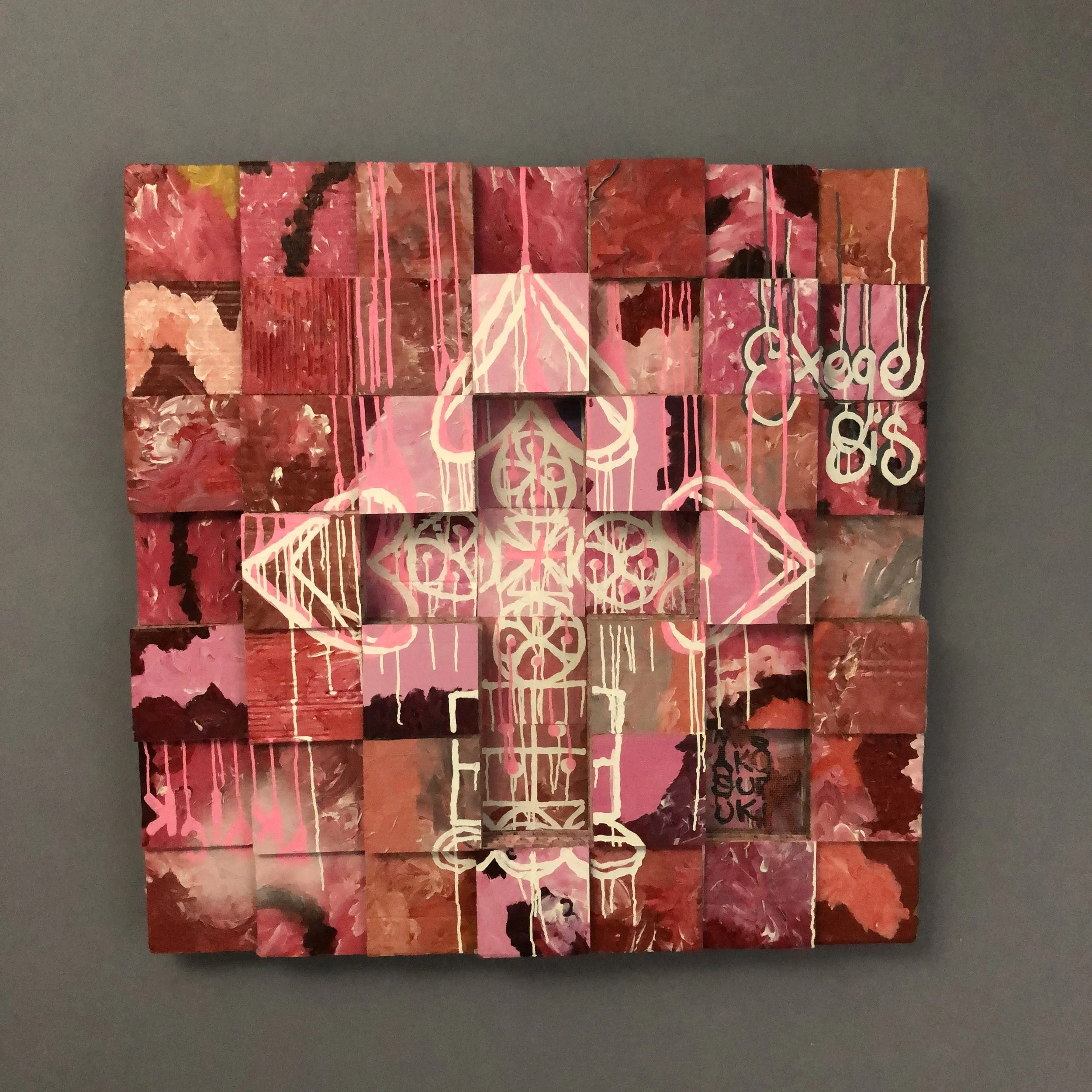 A large grid using cardboard painted squares, featuring various shades of pink and red with white graffiti-style Ethiopian crucifix design in the center and the word "EXEGESIS" and "PKDICK" on the upper right/lower left respectfully.