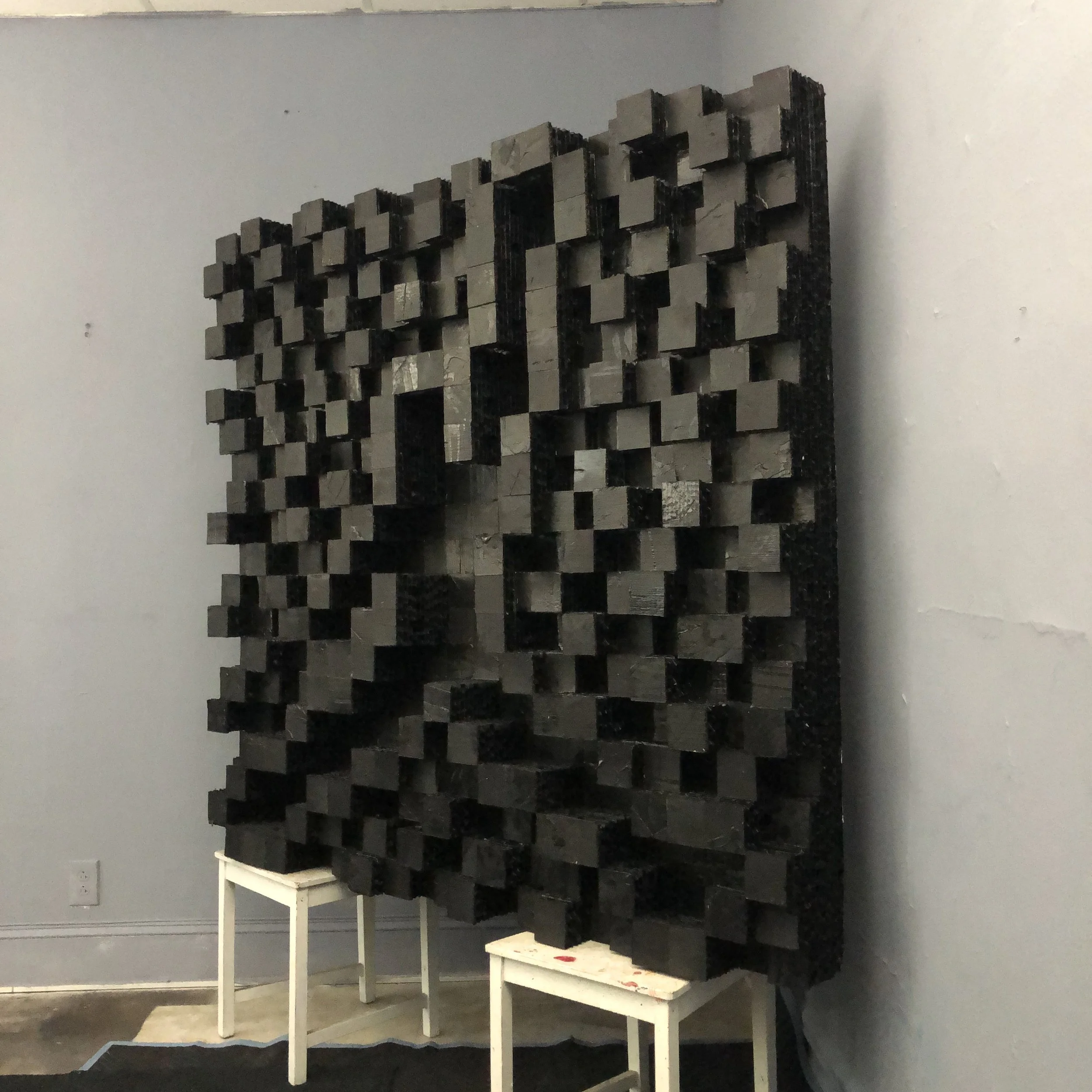 A mixed-media 3D collage art piece composed of cardboard squares, all painted black and arranged in a "AIR JORDAN" design, with the logo recessed into the center of piece.