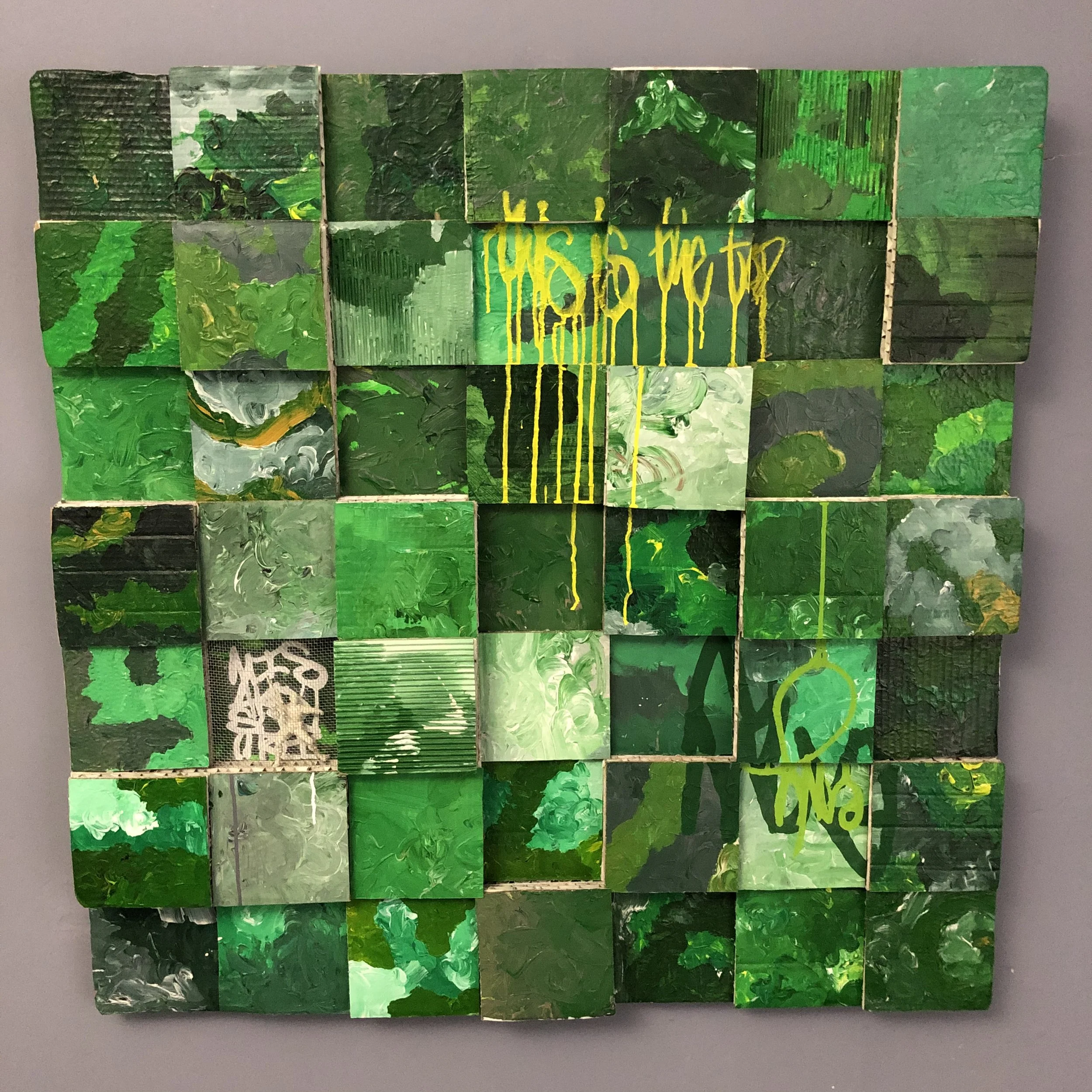 A large grid using cardboard painted squares, featuring various shades of green with yellow and green graffiti-style markings.
