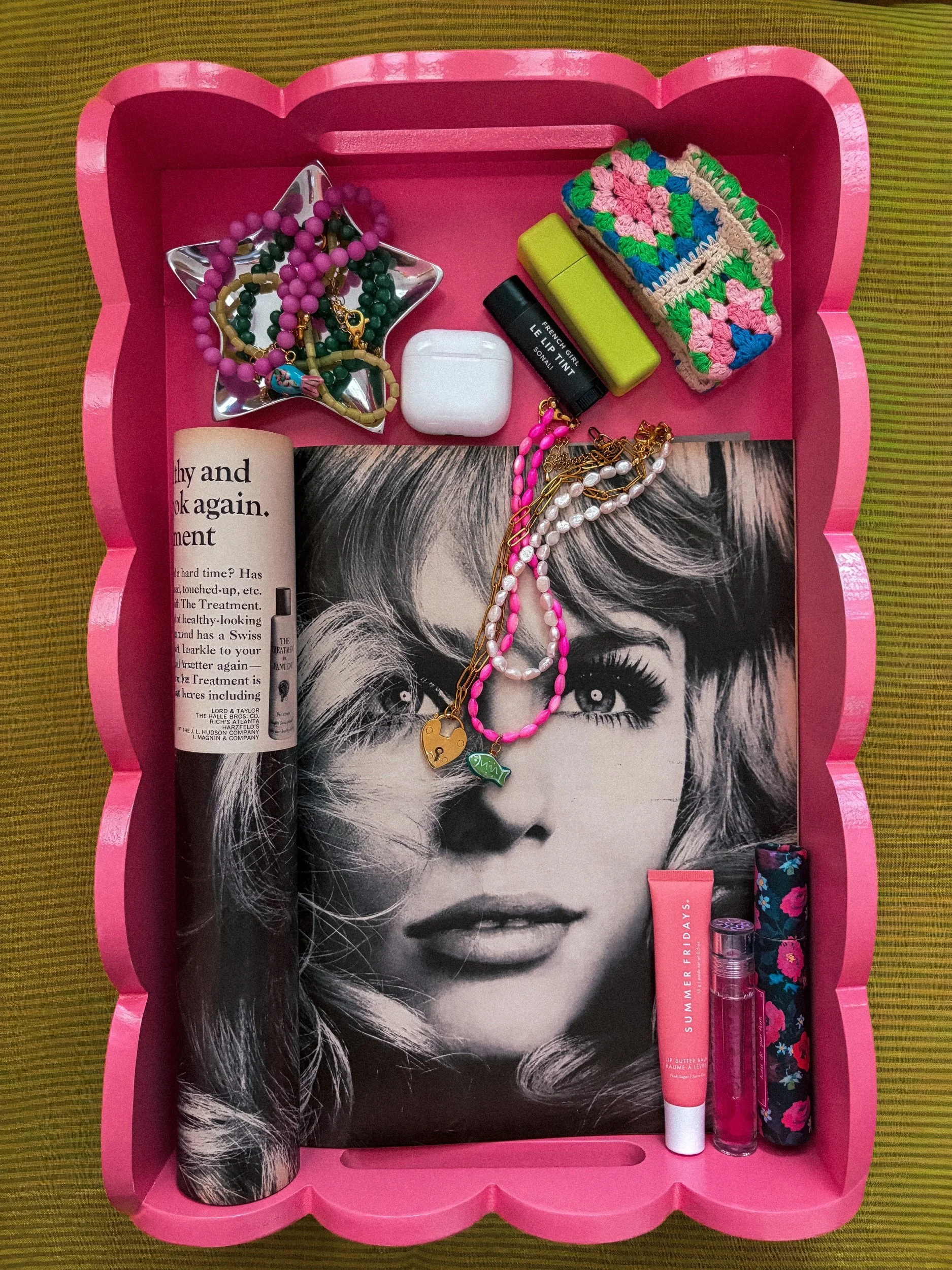 Pink gift box with a black and white photo of a woman's face on the inside lid, jewelry including beaded necklaces, lip balm, lipstick, and small perfume bottles inside.