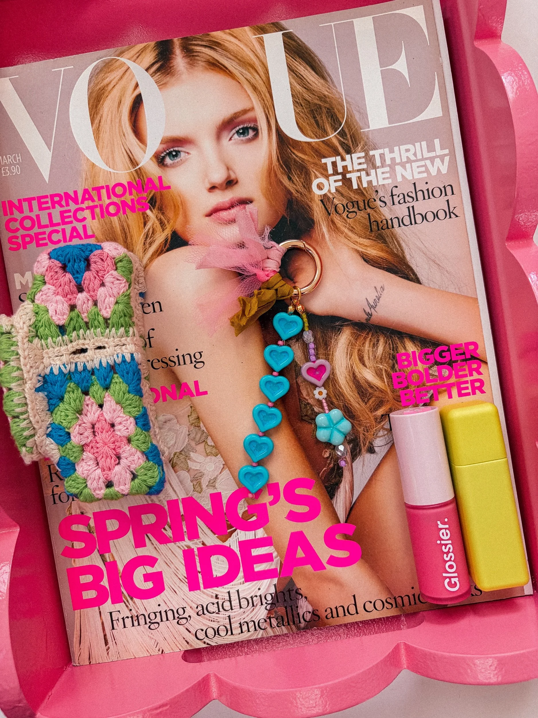 A magazine titled Vogue with a cover image of a woman with long, wavy red hair and blue eyes. The cover has pink and white text, including headlines about fashion and big ideas for spring.
