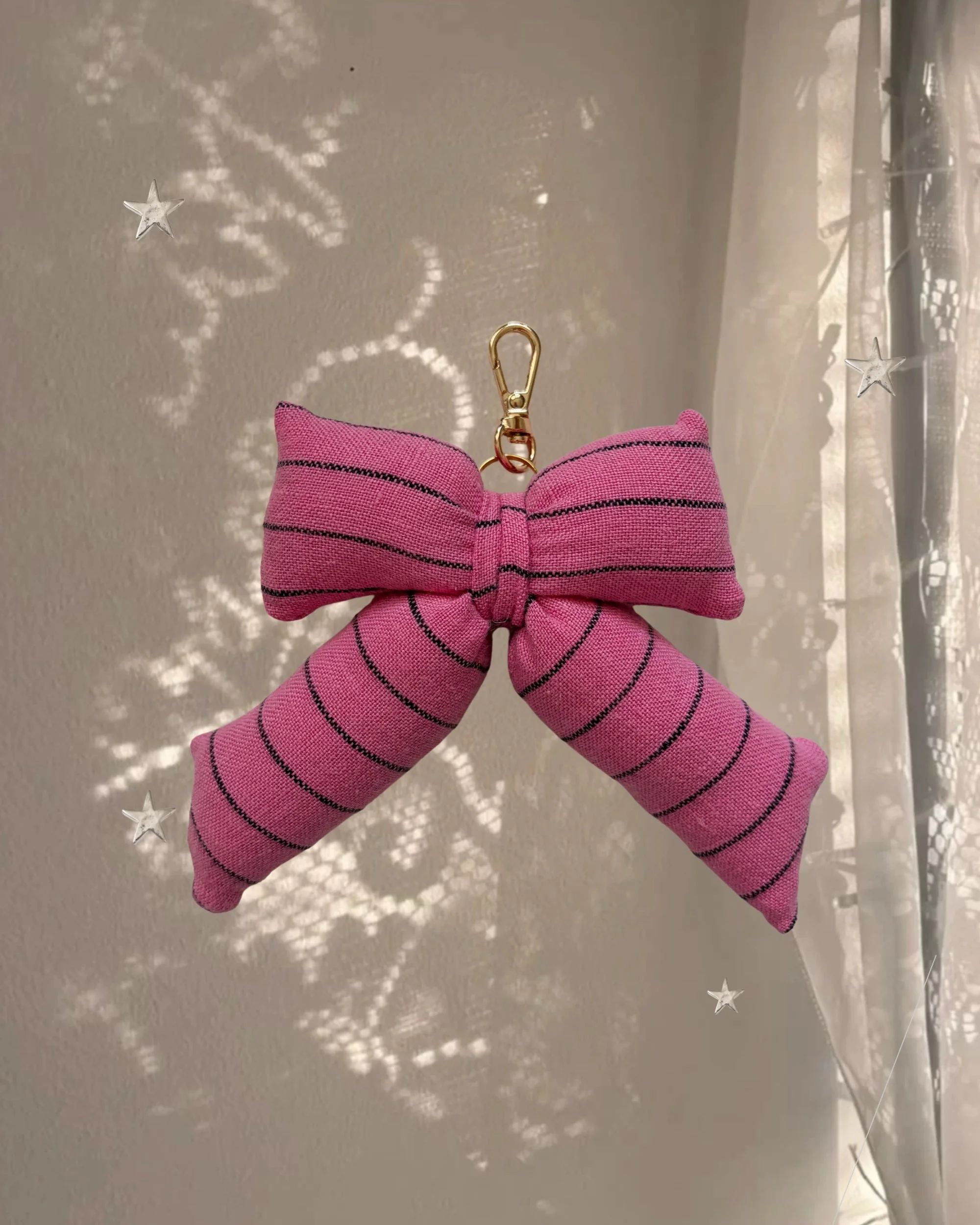 Berry Striped Puffy Bow Bag Charm hanging in front of a sheer curtain with sparkly star-shaped light