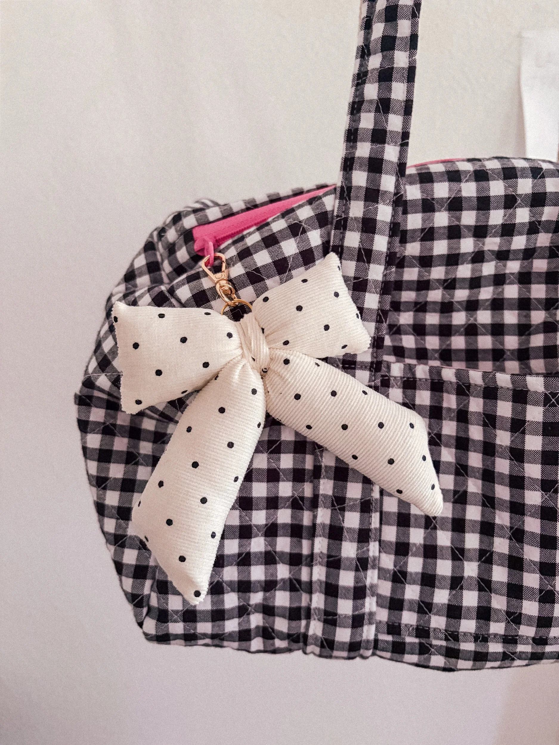 Cream polka dot puffy bow bag charm on a black and white gingham bag with a pink zipper