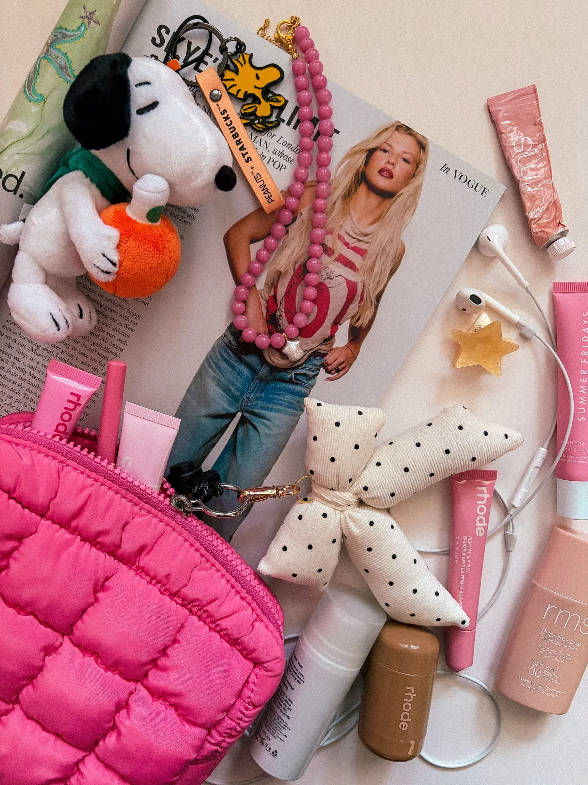 Black and white polka dot bow bag charm in a flat lay with a quilted pink pouch and pink accessories
