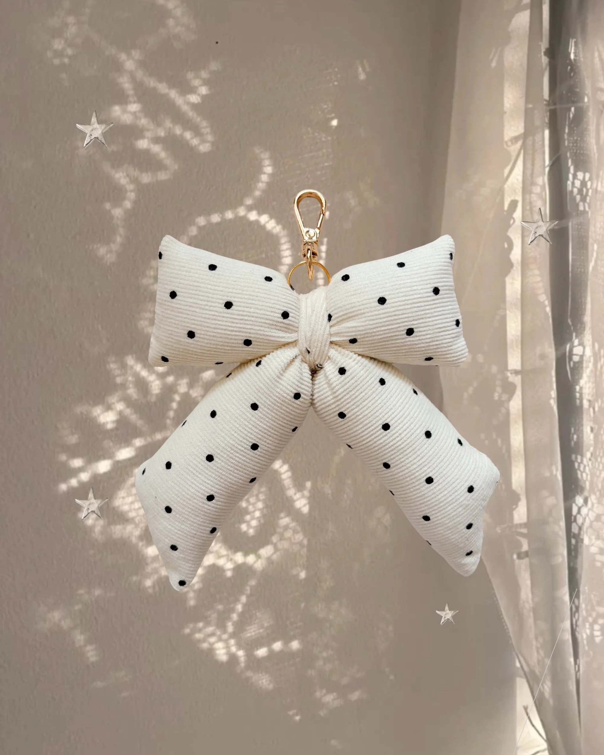 Black Dot Puffy Bow Bag Charm hanging in front of a sheer curtain with sparkly star-shaped light
