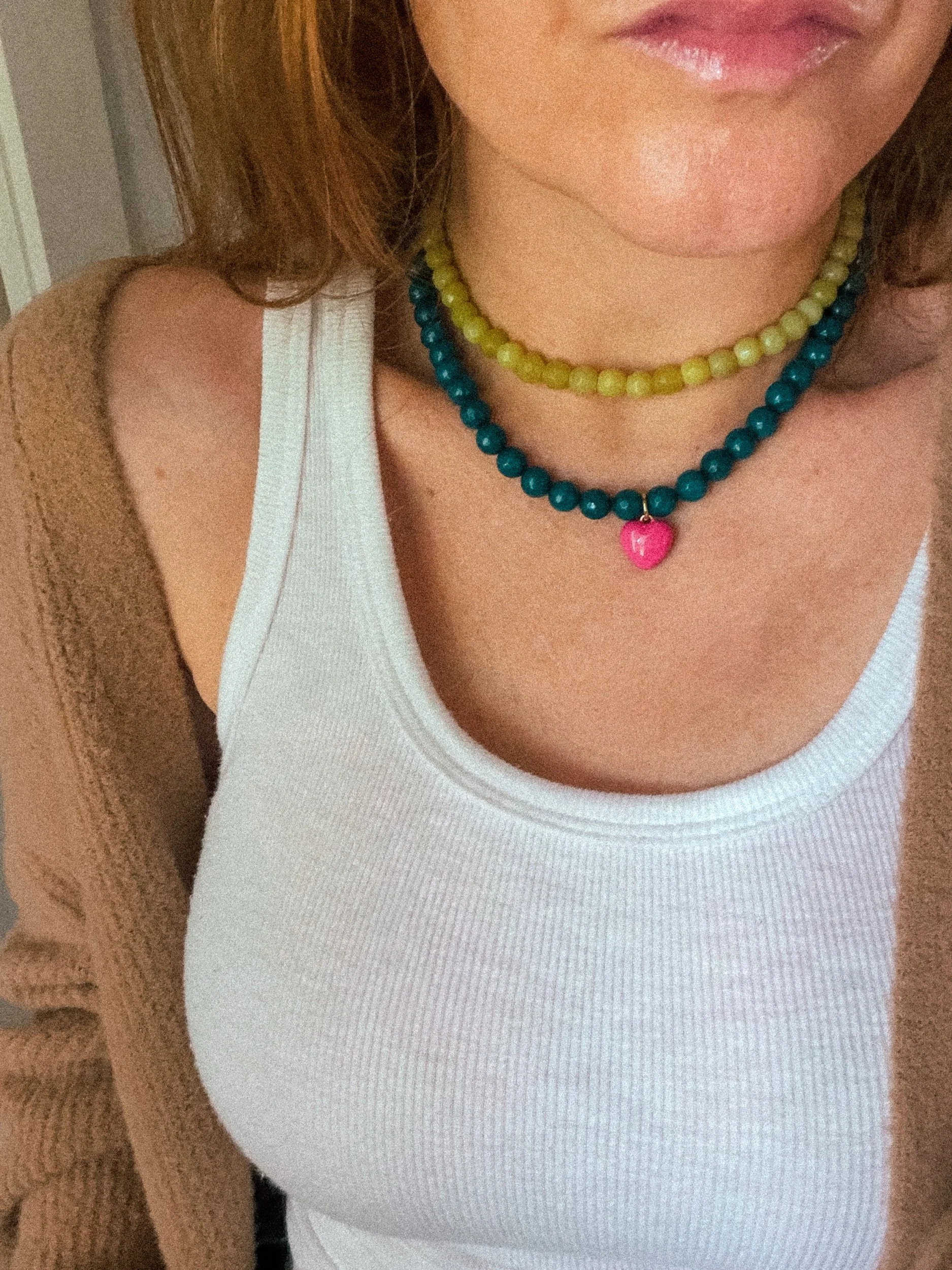 Chartreuse Glow Beaded Necklace layered with a teal heart charm necklace, worn with a white tank top and brown knit cardigan