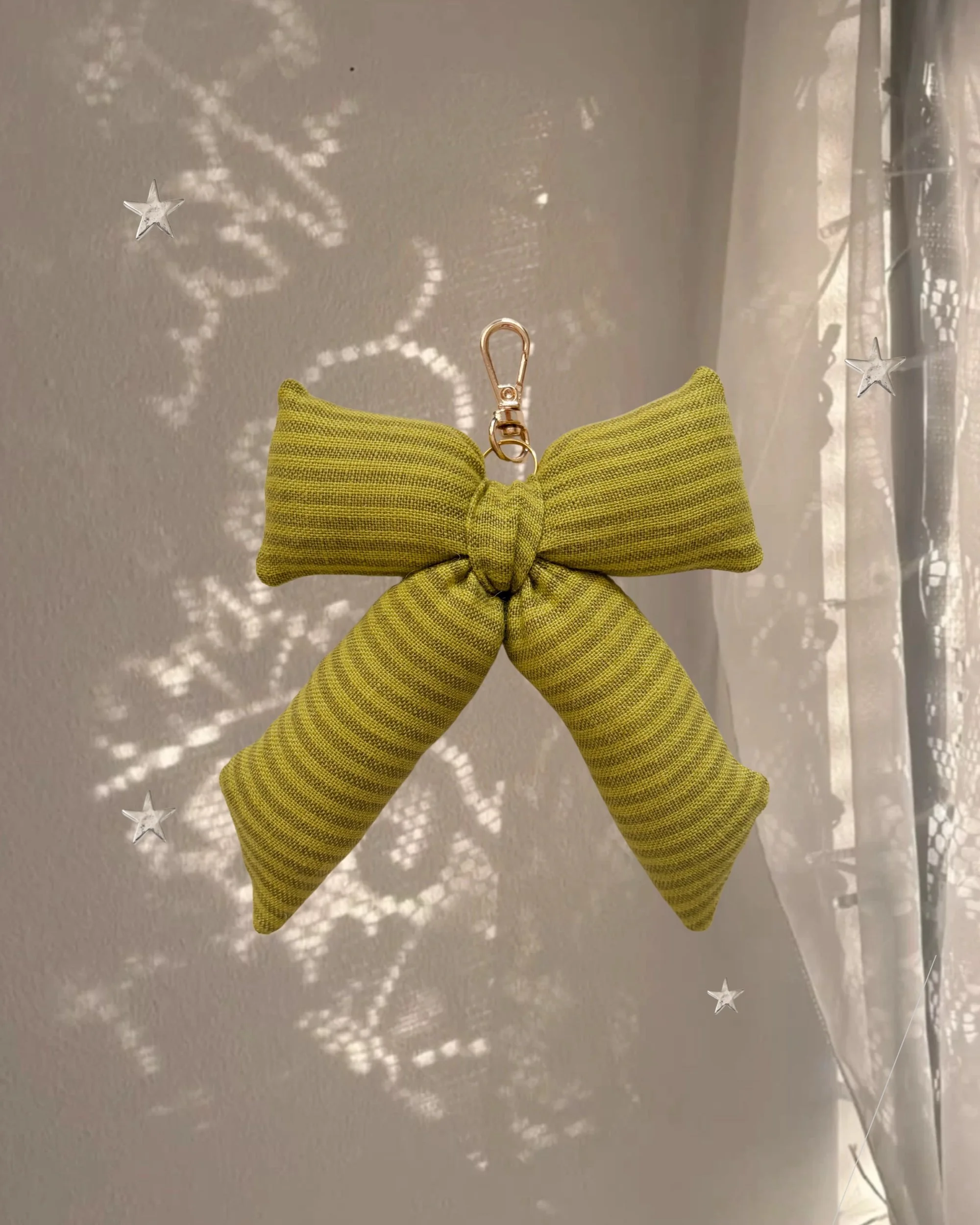 Chartreuse Stripe Puffy Bow Bag Charm hanging in front of a sheer curtain with sparkly star-shaped light