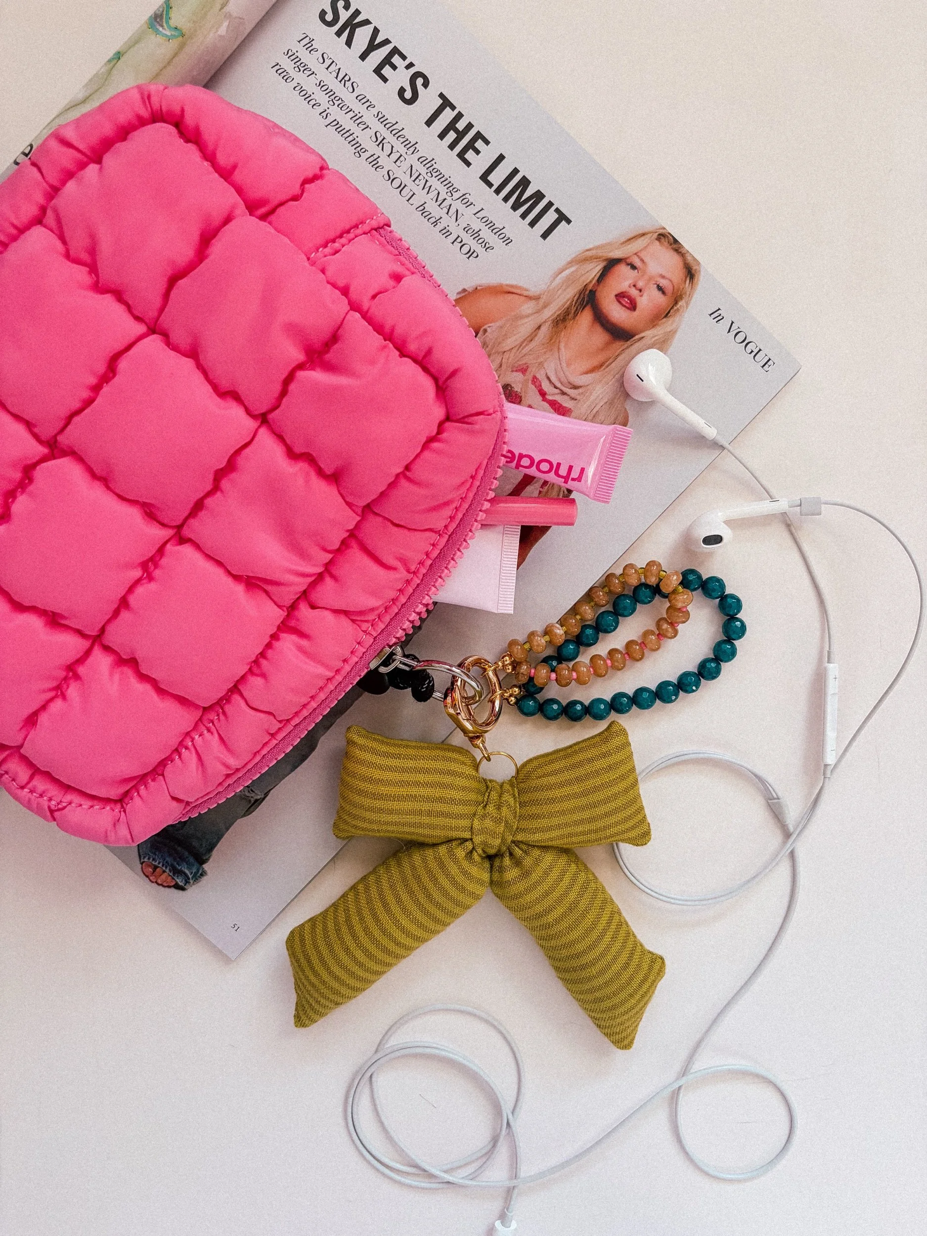 Chartreuse green striped puffy bow bag charm clipped to a quilted pink pouch with a teal and amber beaded charm
