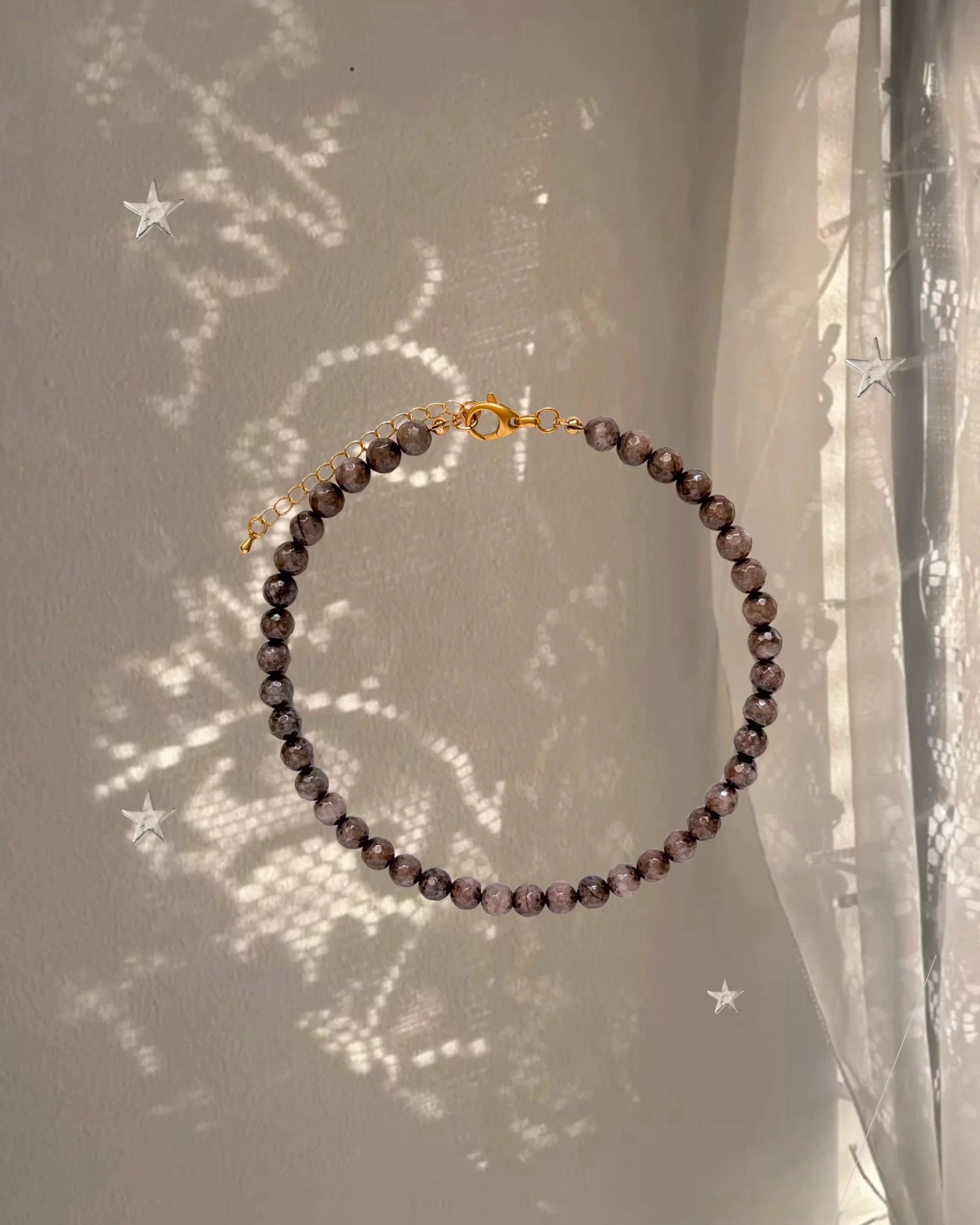 Chestnut Brown Beaded Necklace with gold clasp hanging in front of a sheer curtain with sparkly star-shaped light