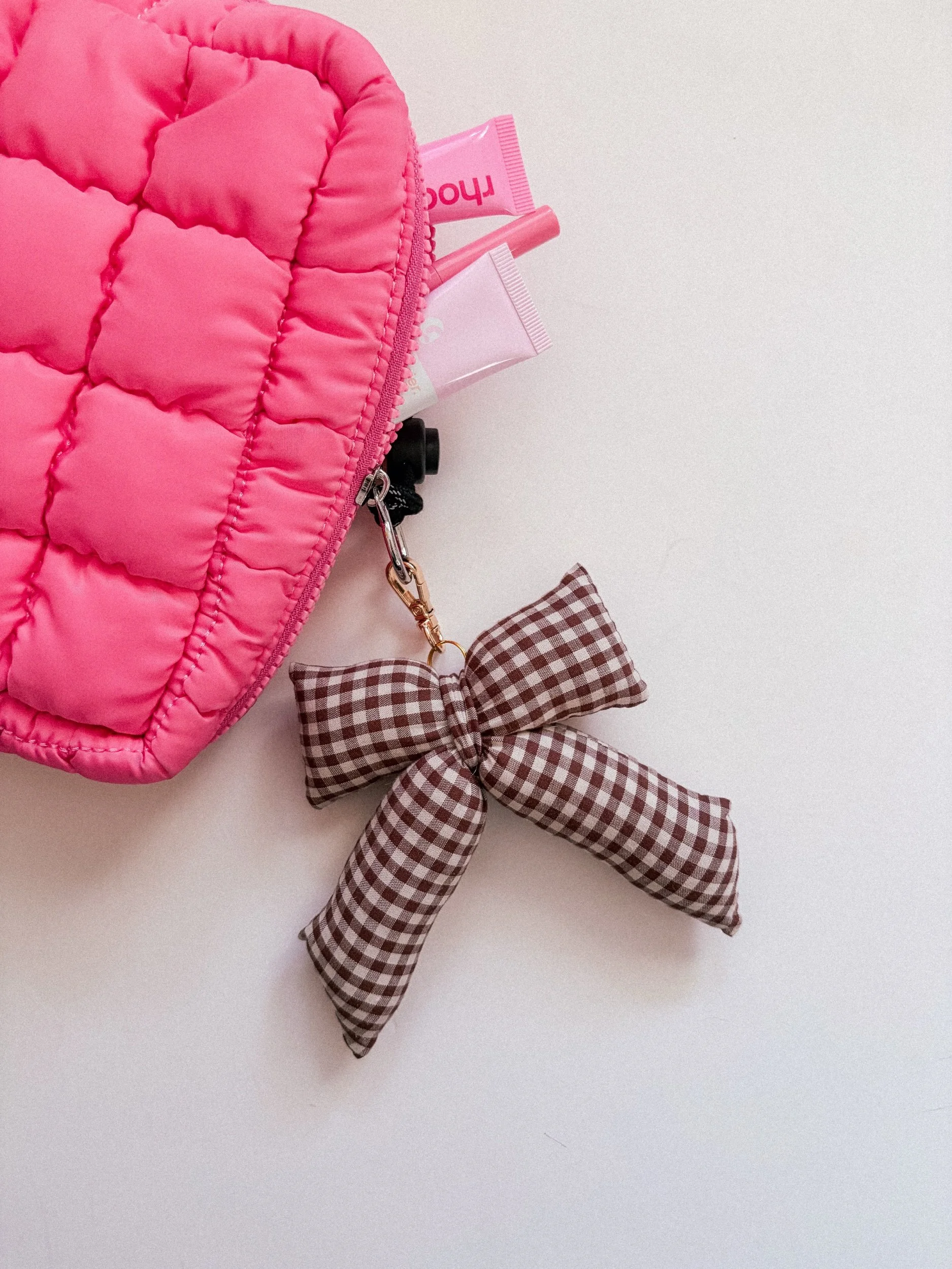 Brown and white gingham puffy bow bag charm clipped to a quilted pink pouch