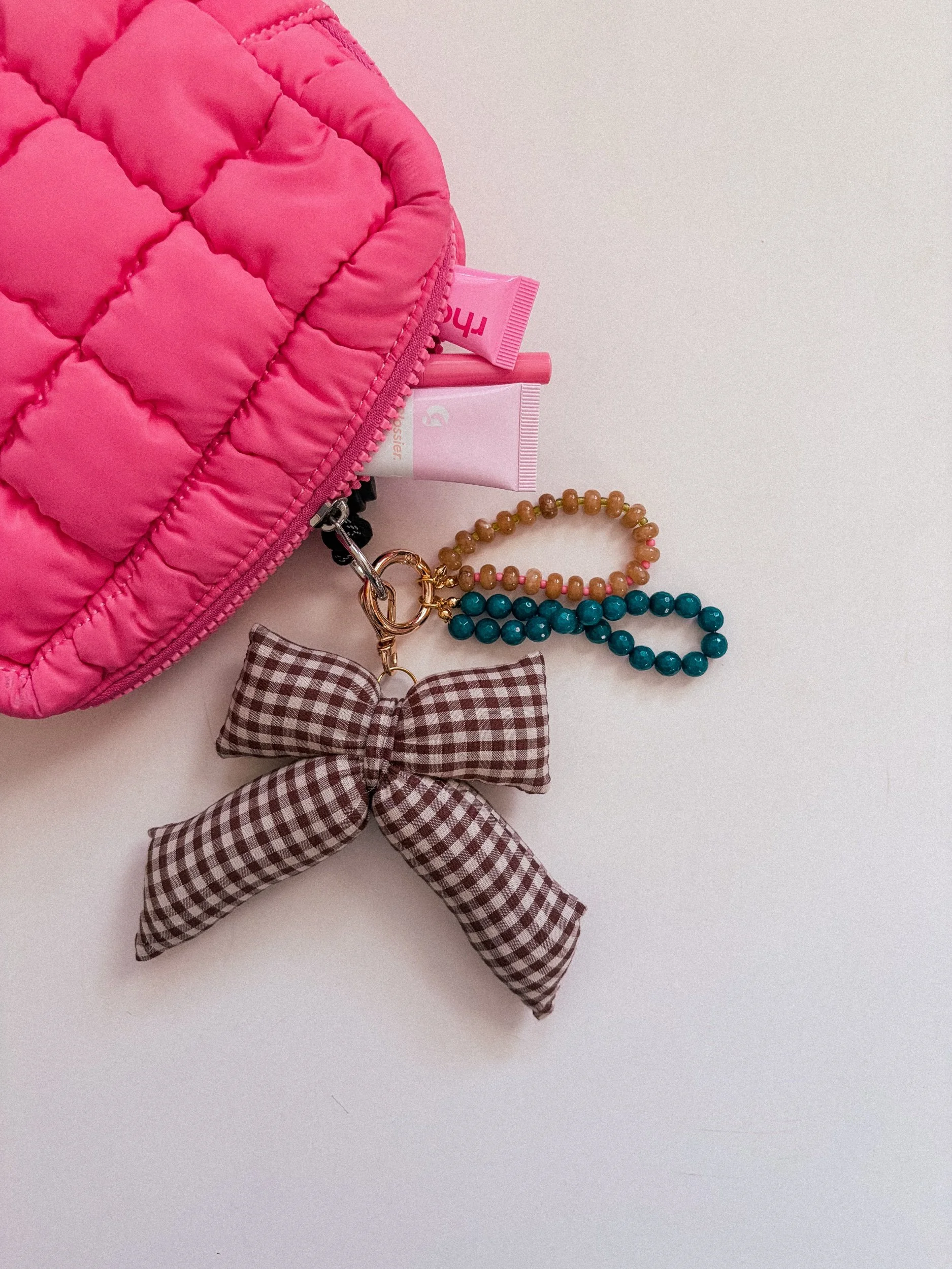Chocolate brown gingham bow charm with a teal and amber beaded charm on a pink puffer pouch