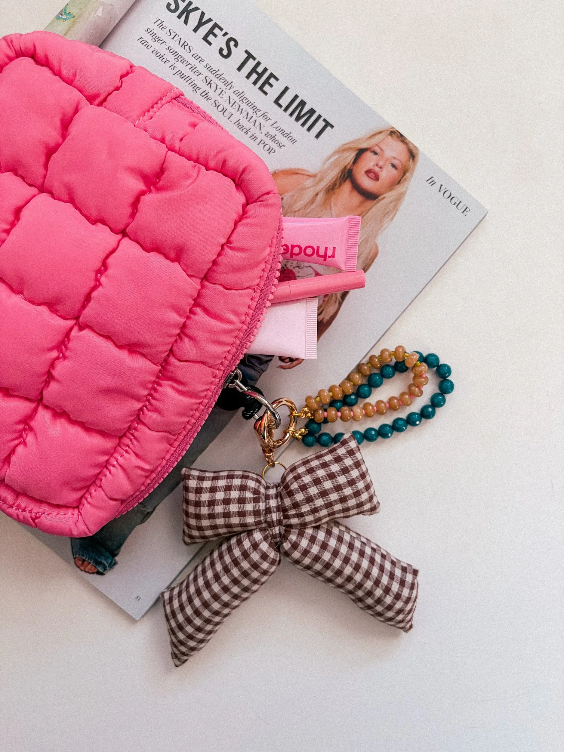 Handmade brown gingham bow bag charm in a flat lay with a quilted pink pouch and a teal and amber beaded charm