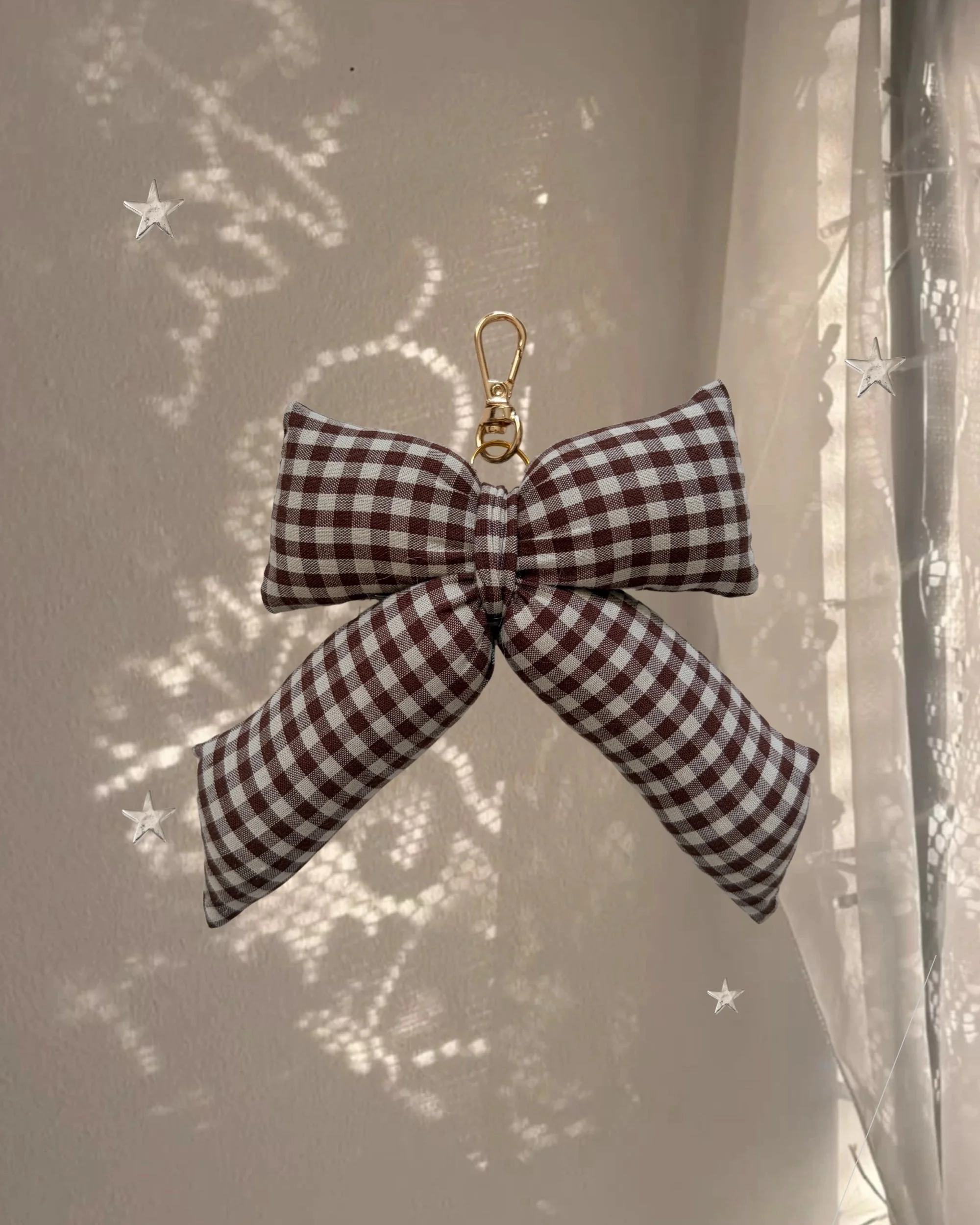 Chocolate Gingham Puffy Bow Bag Charm hanging in front of a sheer curtain with sparkly star-shaped light