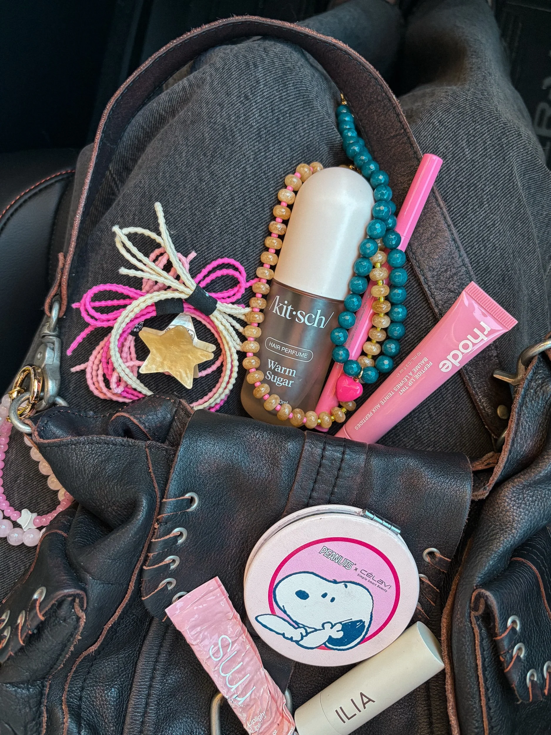 Tan beaded necklace with a teal beaded necklace in a flat lay on a black leather bag with pink accessories