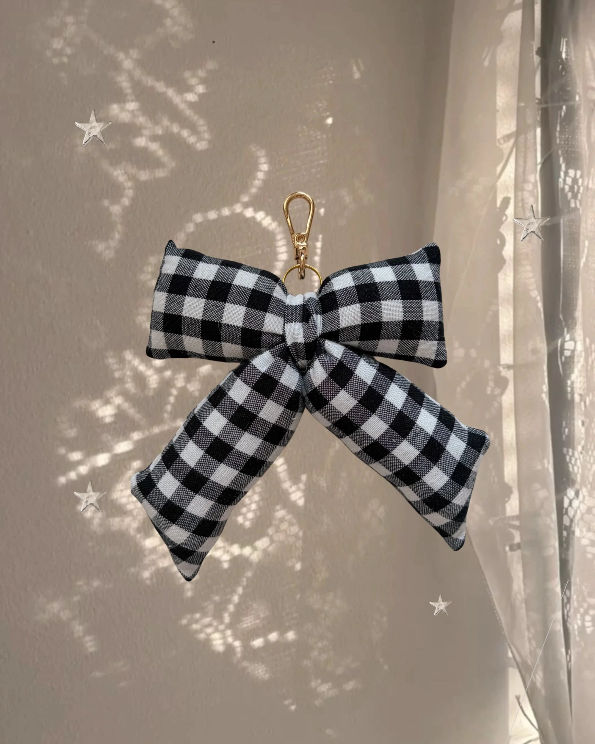 Midnight Gingham Puffy Bow Bag Charm hanging in front of a sheer curtain with sparkly star-shaped light