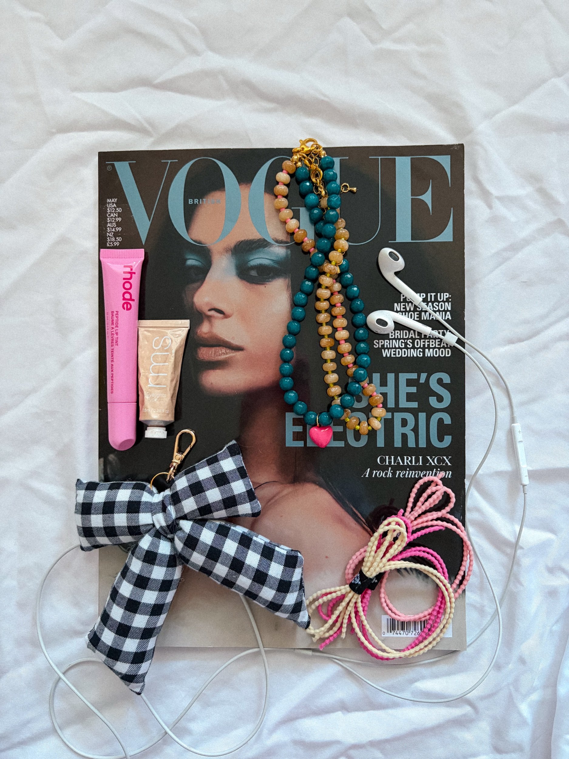Black and white gingham bow bag charm in a flat lay with teal and amber beaded charms on a white background