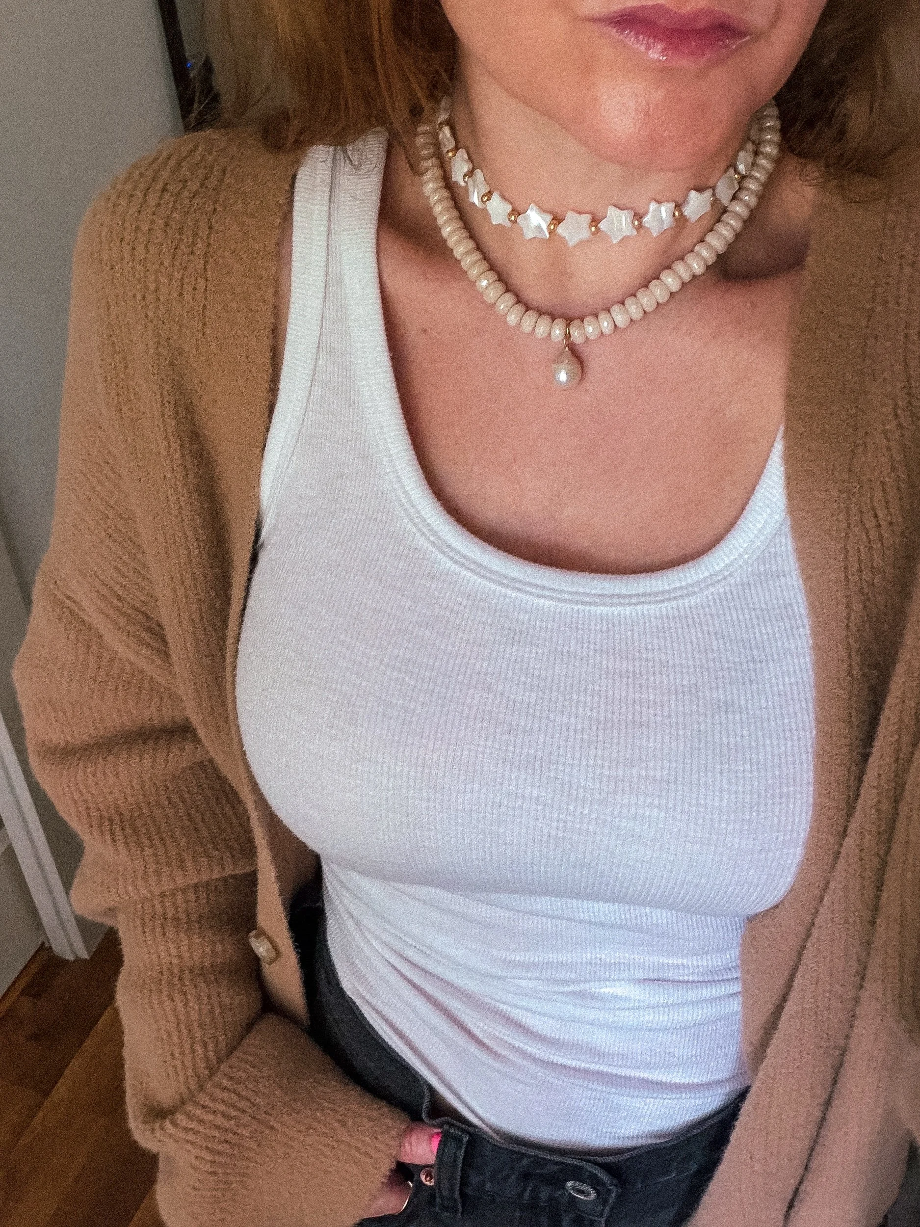 Cream beaded necklace with pearl drop layered with a white star bead choker, worn with a white tank top and brown cardigan