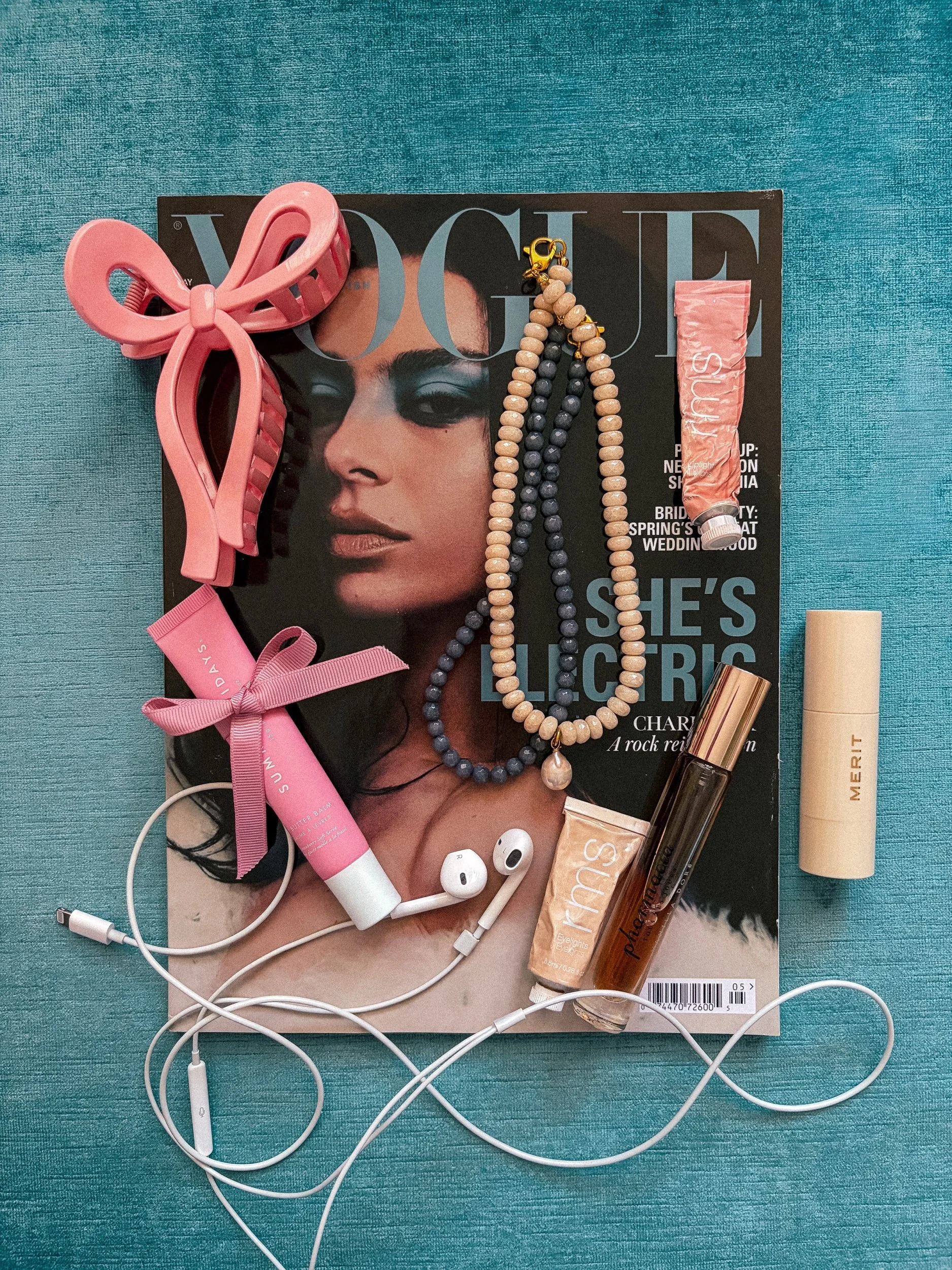 Handmade gray beaded necklace styled in a flat lay on a teal background with a pink bow claw clip and earbuds