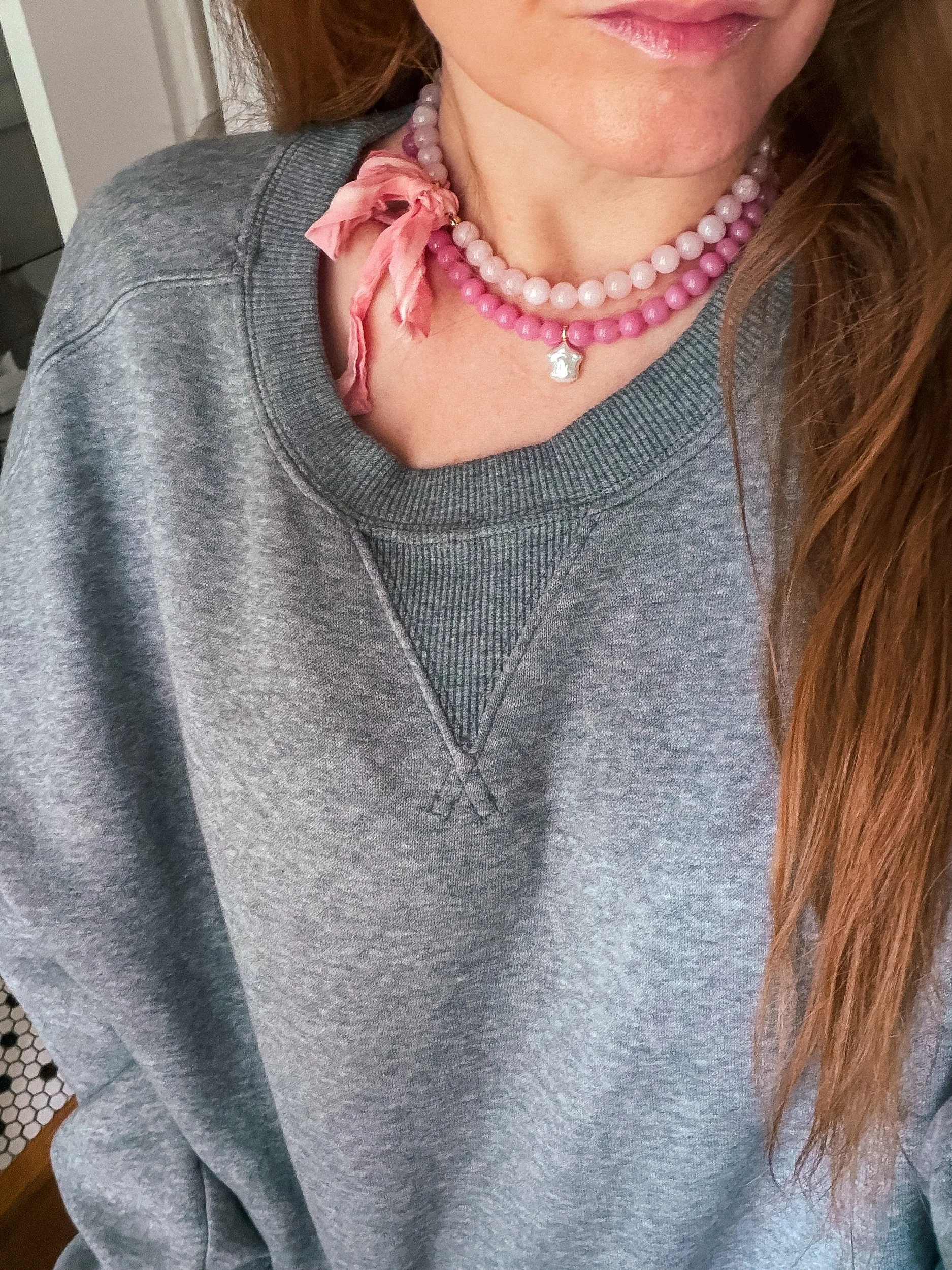 Pink beaded necklace layered with a hot pink charm necklace, worn with a gray crewneck sweatshirt