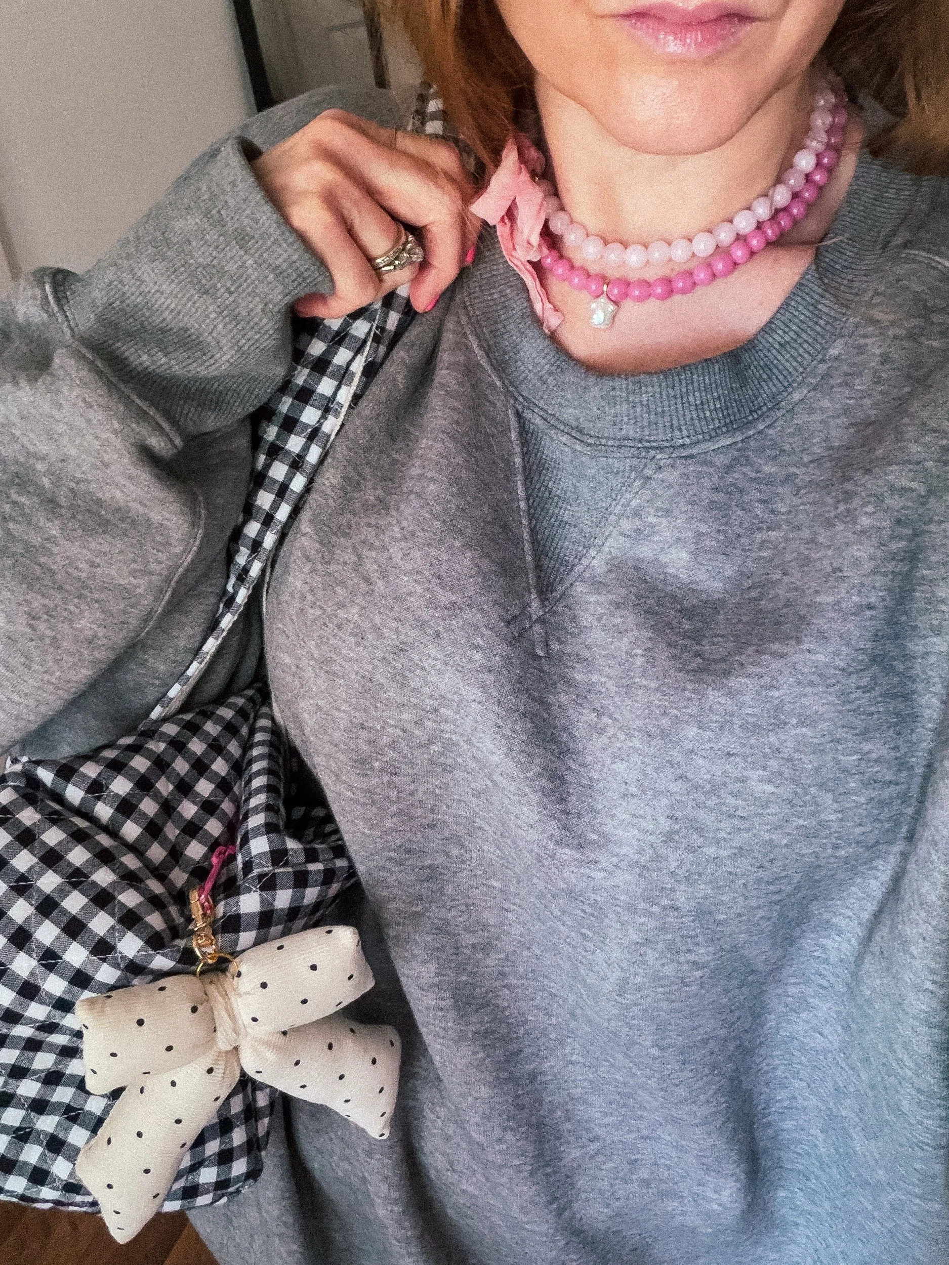 Pink beaded necklace stack with ribbon bow worn with a gray sweatshirt and gingham bag
