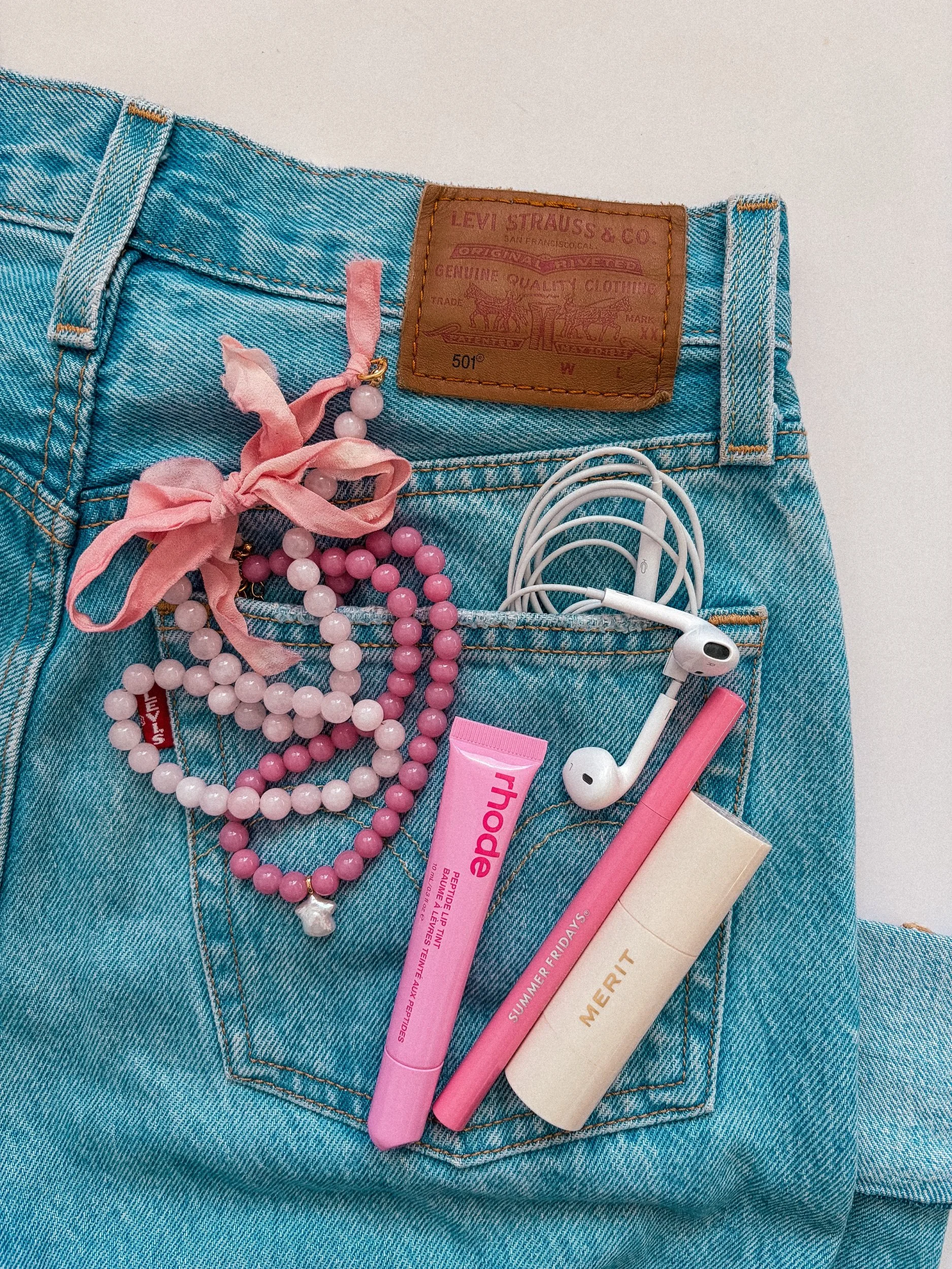 Petal Blush Bow Beaded Necklace with pink ribbon bow in a flat lay on a denim back pocket