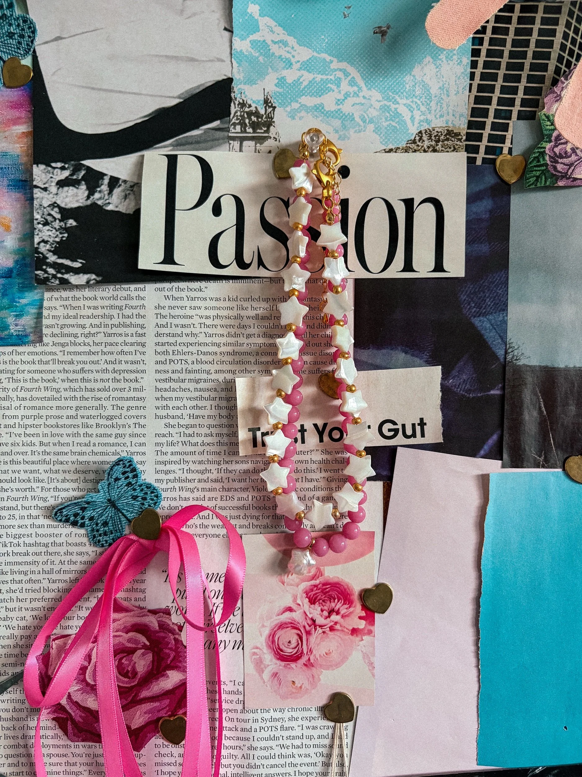 Pink beaded necklace with white star beads draped over a pink and blue magazine collage with ribbons
